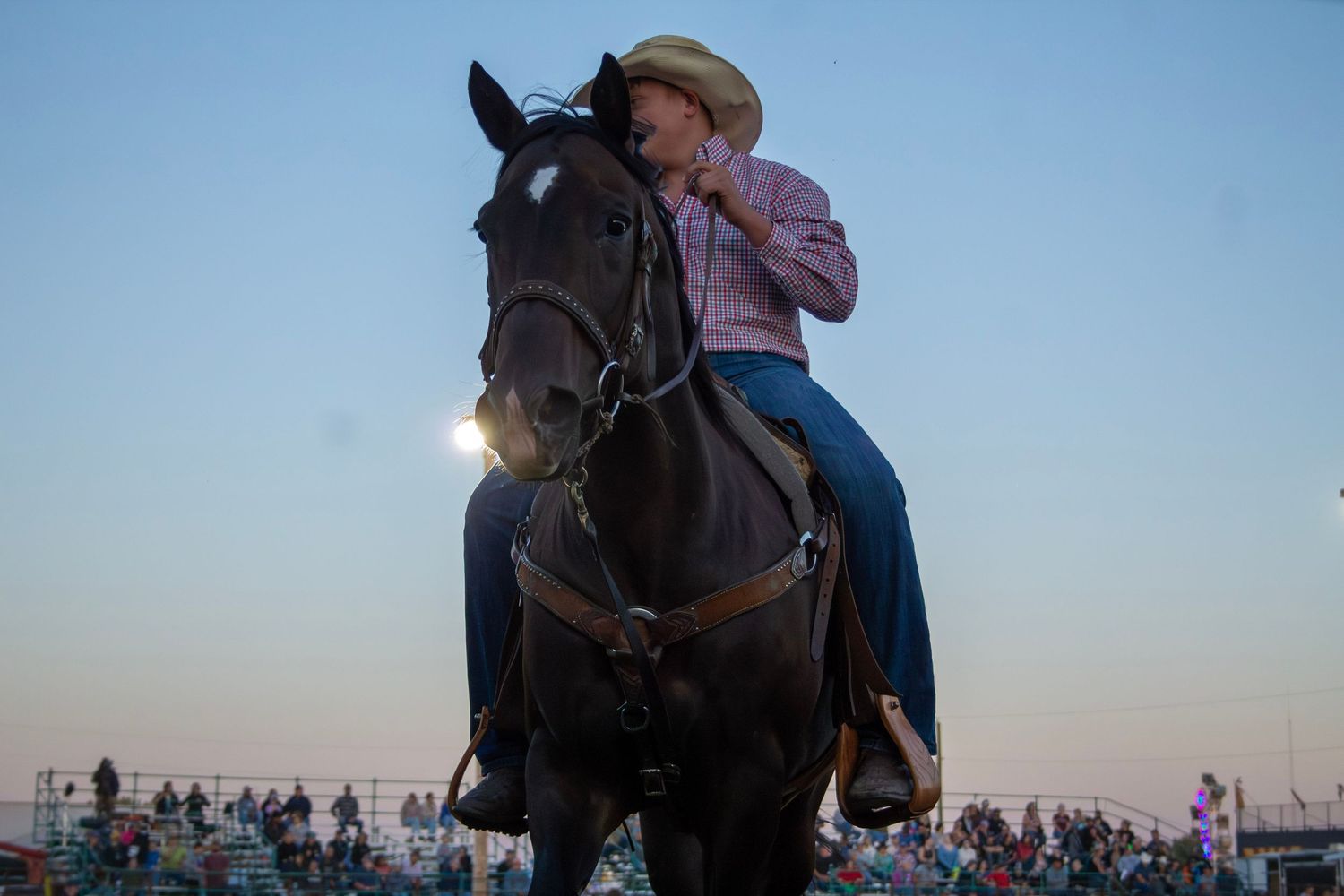 A group of equestrians ride horses in formation during a sunset performance at a rodeo arena.