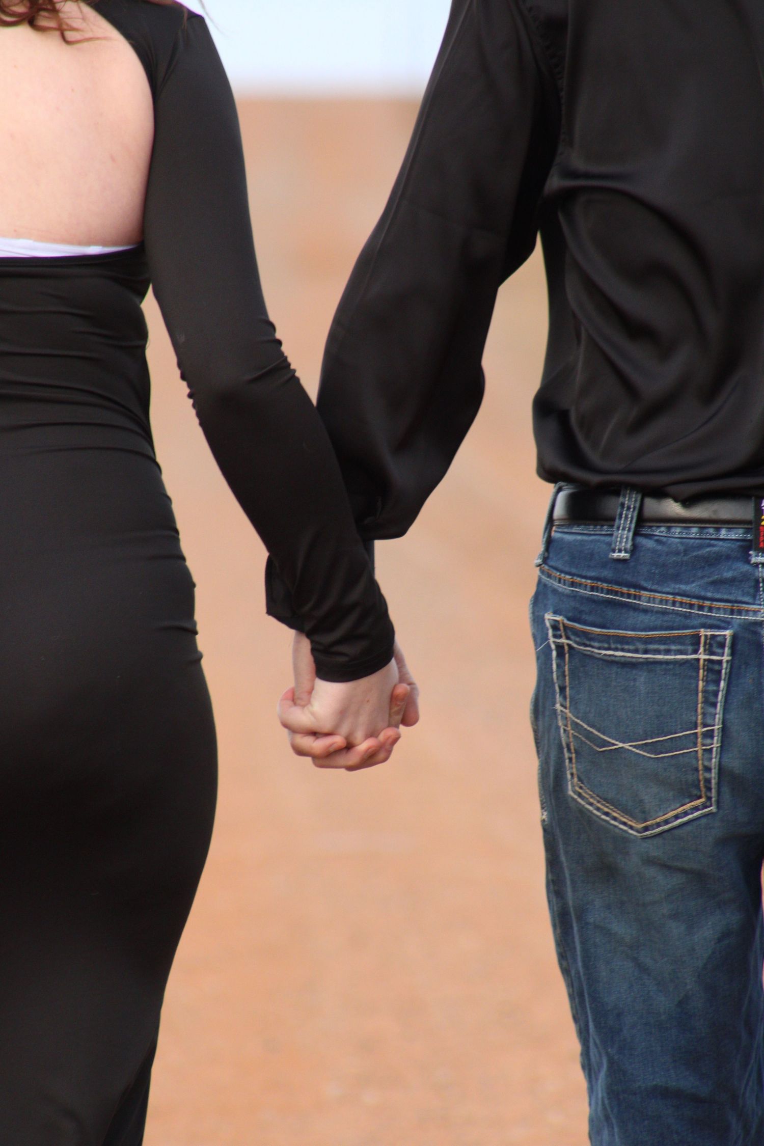 Close-up view of two people holding hands wearing contrasting black top and blue jeans against neutral background.
