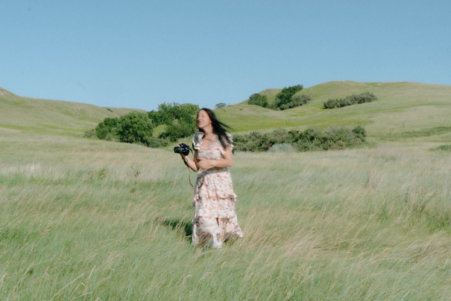 Rolling green hills with figure in floral dress walking through tall grass meadow.