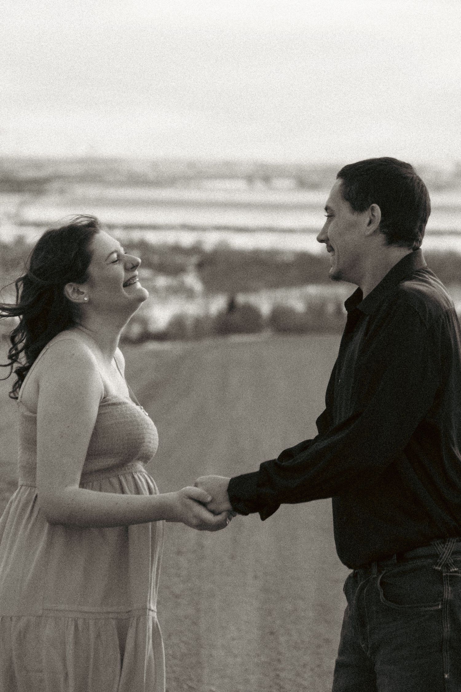 A couple in a field shares a romantic moment as the woman in a white dress reaches toward her partner in black.