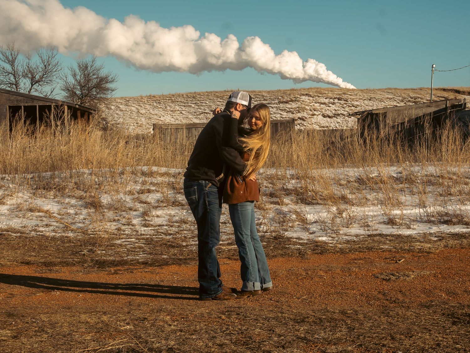 Two people walk together on a snowy winter trail through a scenic mountain landscape on a sunny day.