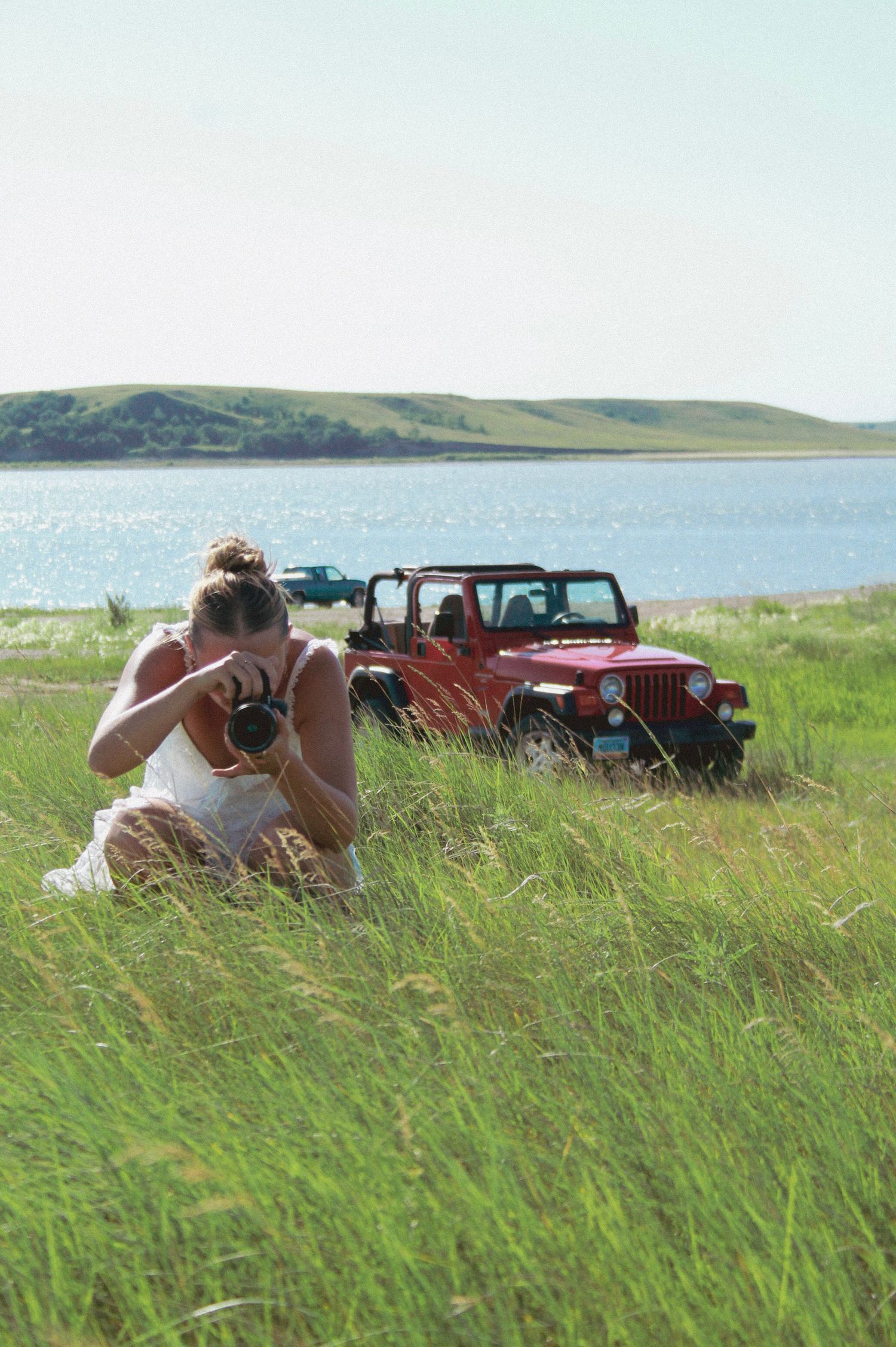 Red Jeep parked on grassy hill overlooking coastal waters.