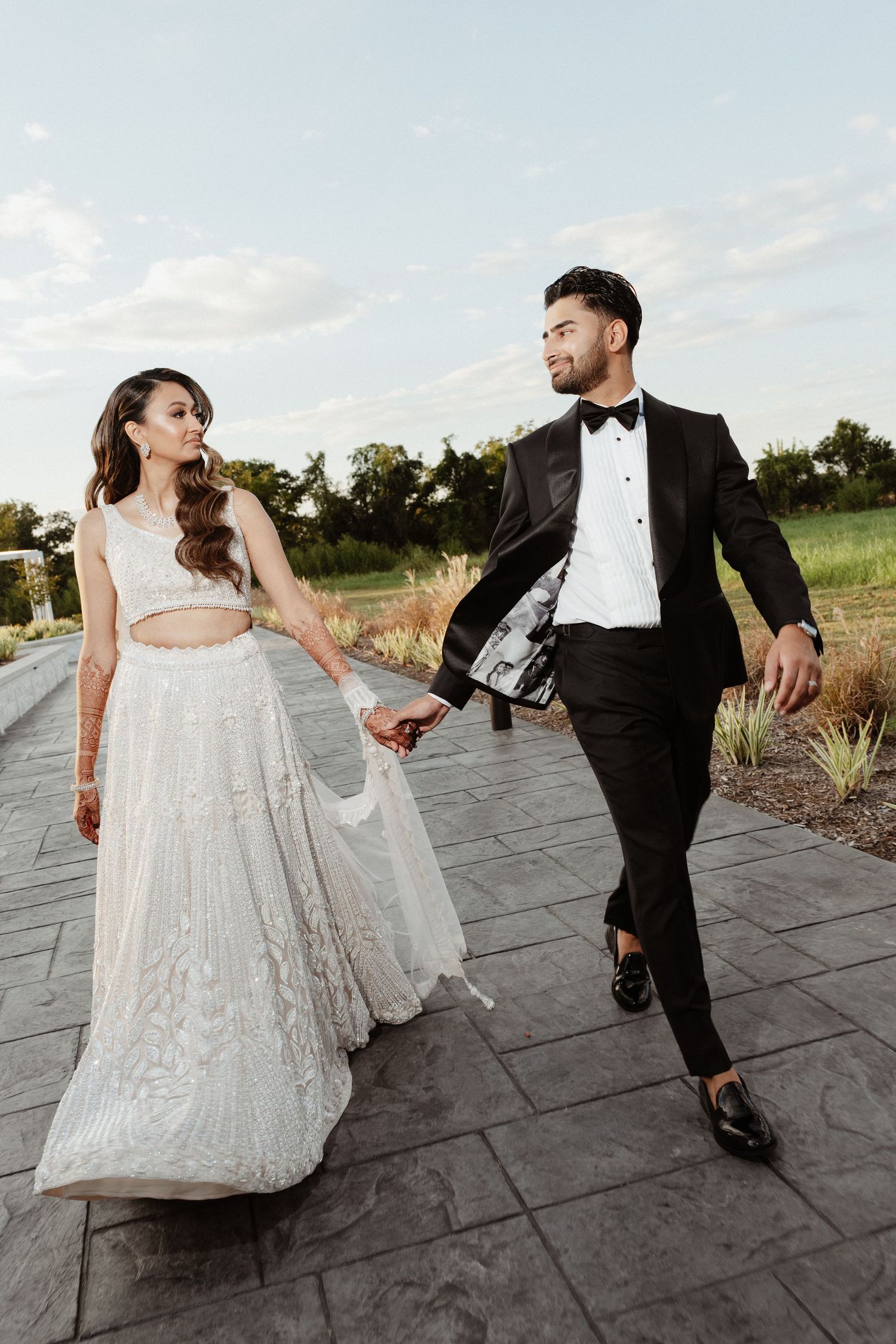 A couple in wedding attire dances and laughs together on a stone patio with a scenic outdoor backdrop at sunset.