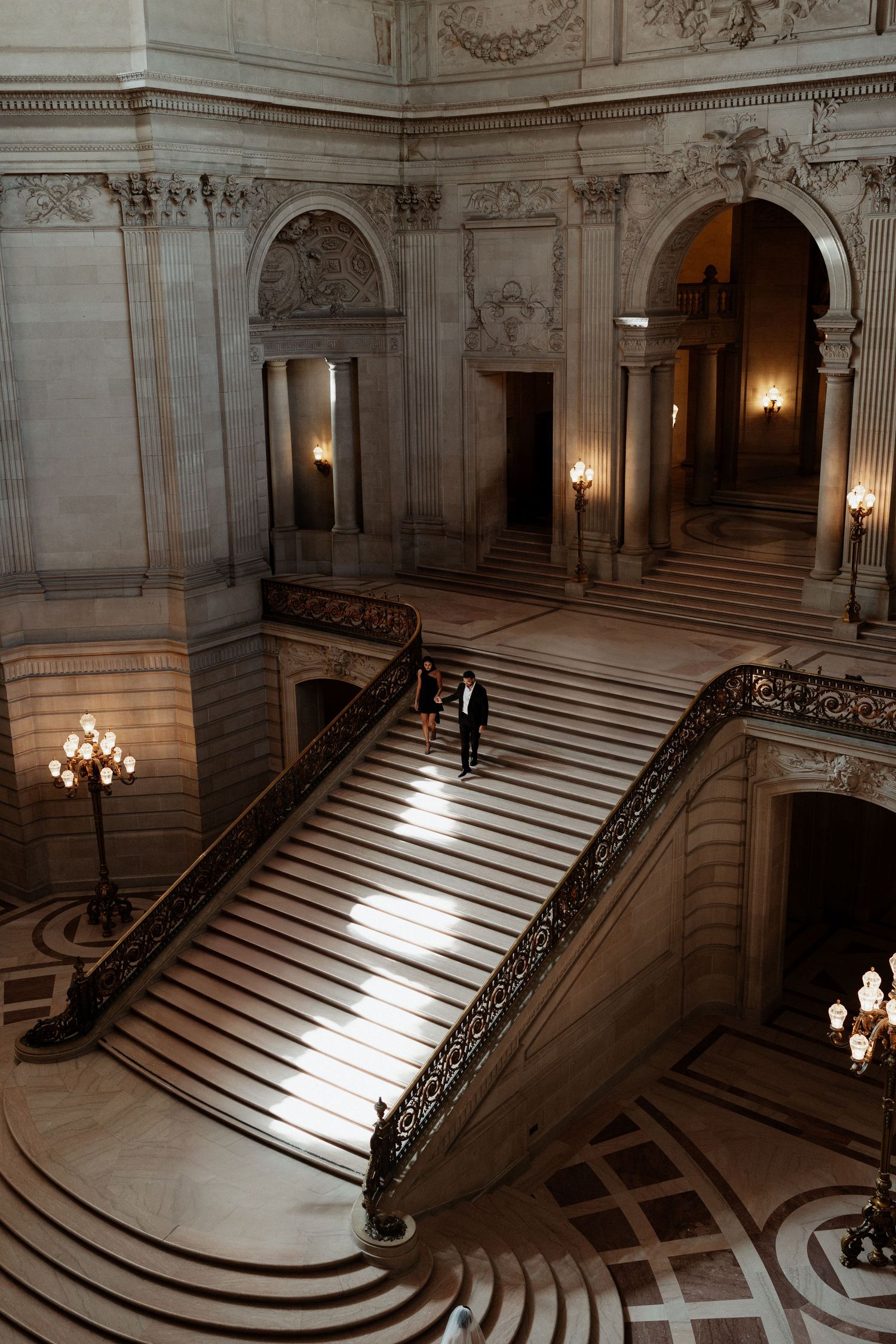 A grand marble staircase with ornate railings and chandeliers in San Francisco City Hall's elegant interior.