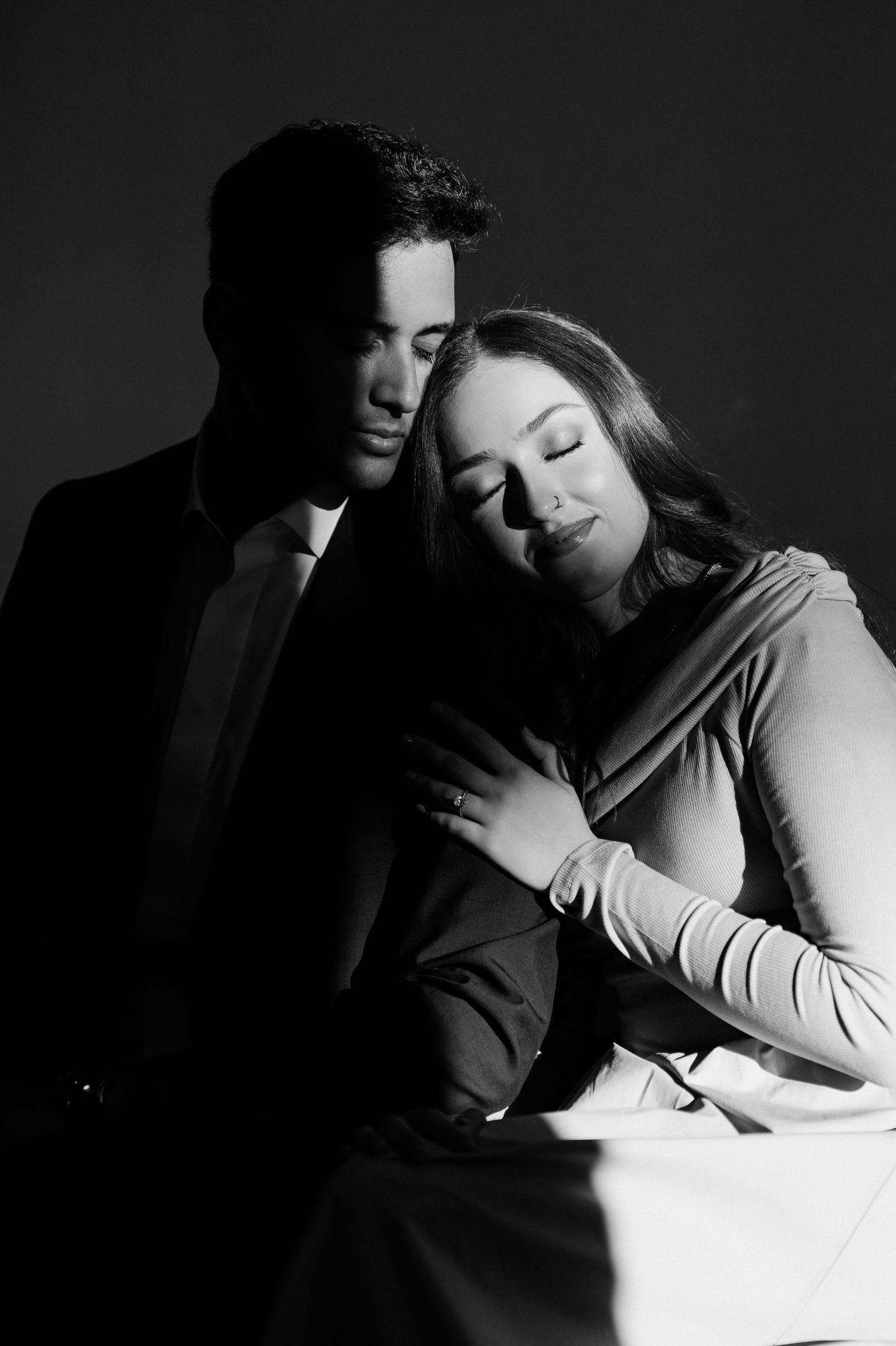 A black and white photo series showing an intimate couple embracing in dramatic shadows and lighting.