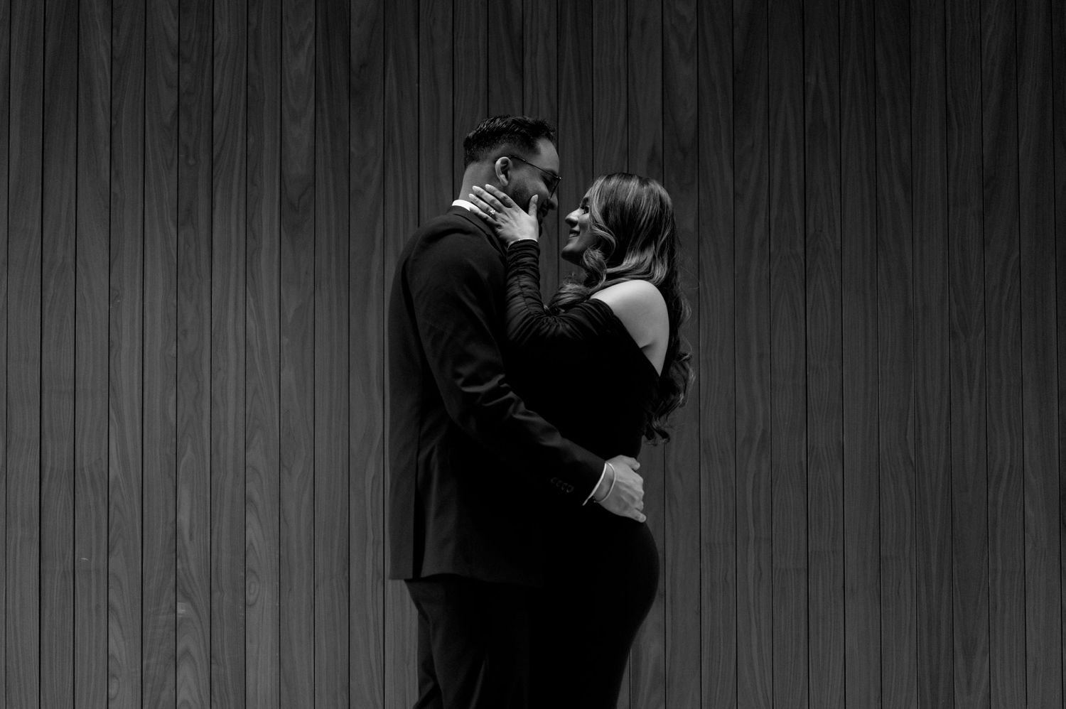 A black and white photograph shows couples dancing together in a dimly lit room with wooden paneled walls.