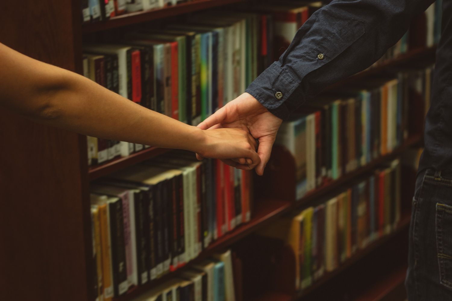 a photo of a man and woman's hands as they walk together in a library