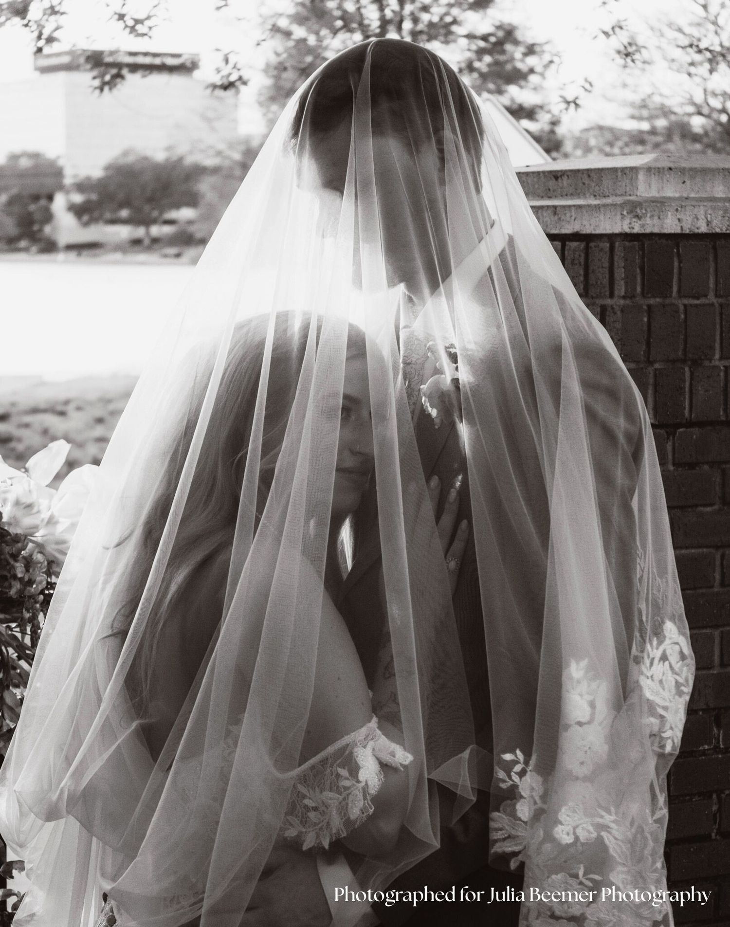 a black and white portrait of a bride and groom under a veil