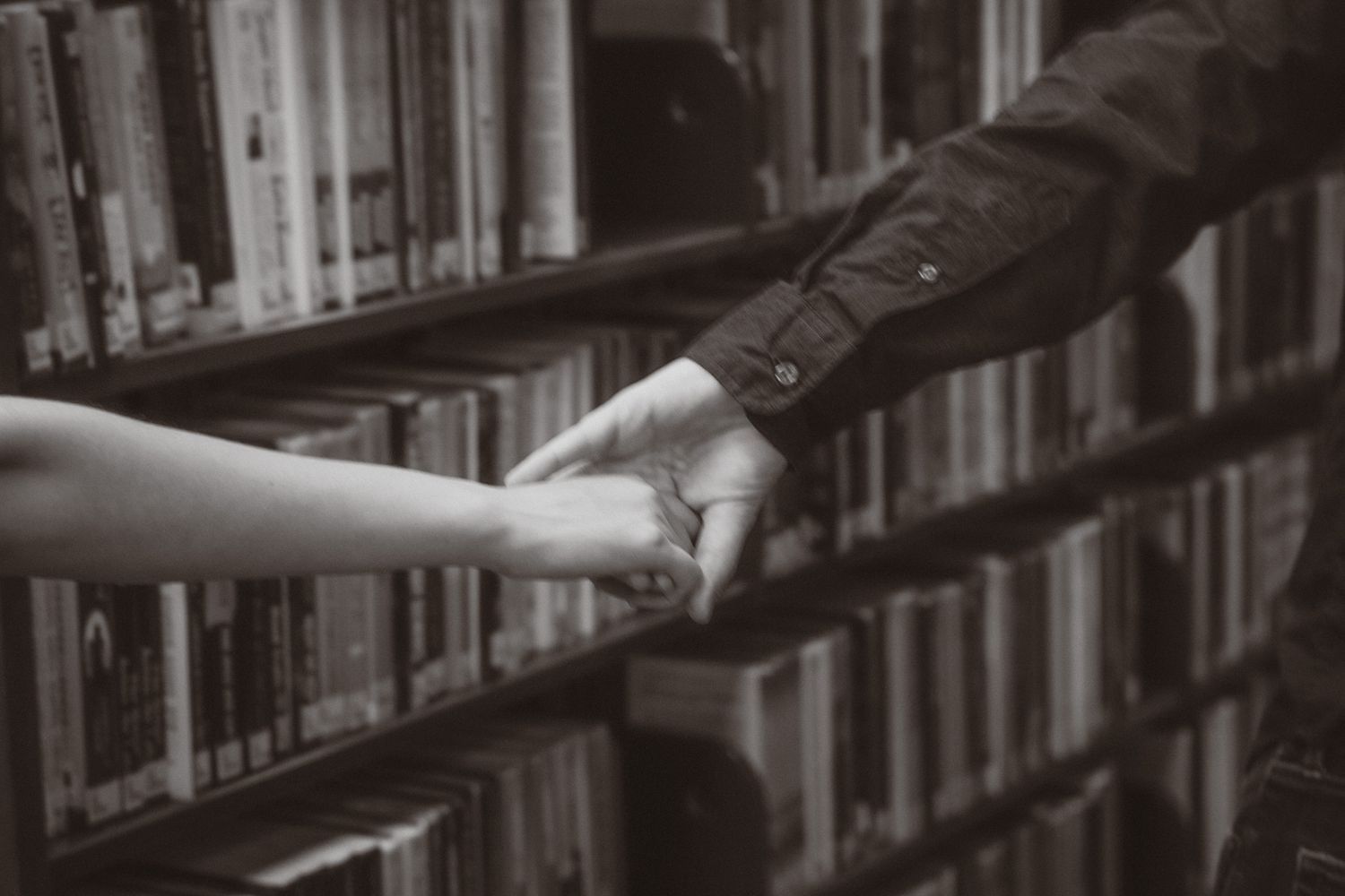 a black and white photo of a couple holding hands as they walk through a library