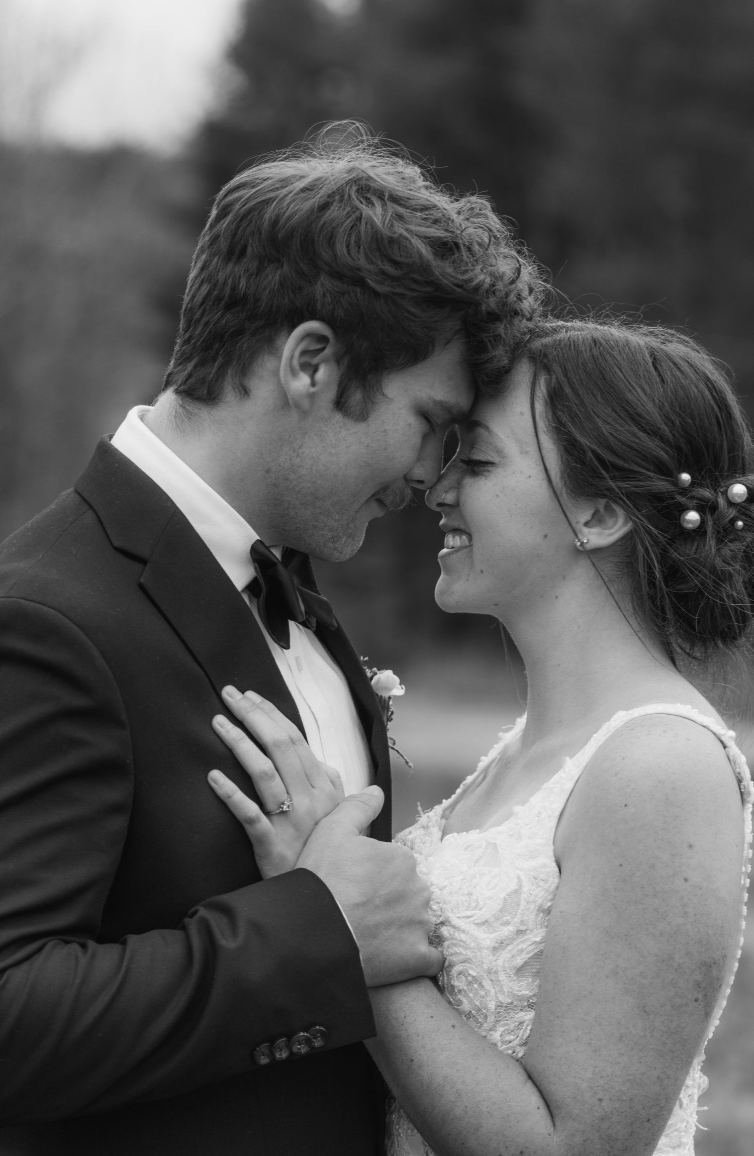 a black and white portrait of a bride and groom smiling at each other - touching foreheads