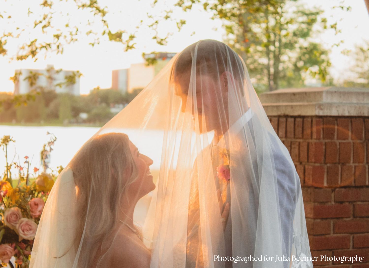 a portrait of a bride and groom looking up at each other under a viel