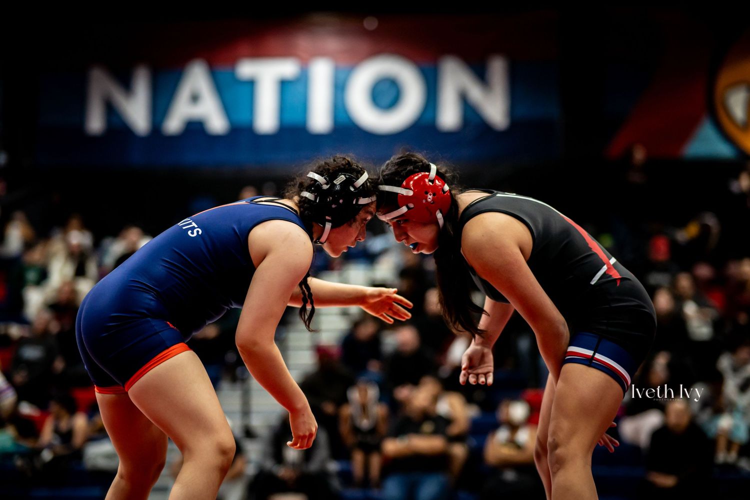 Wrestlers in red and blue uniforms grappling during an intense competitive match on the mat.