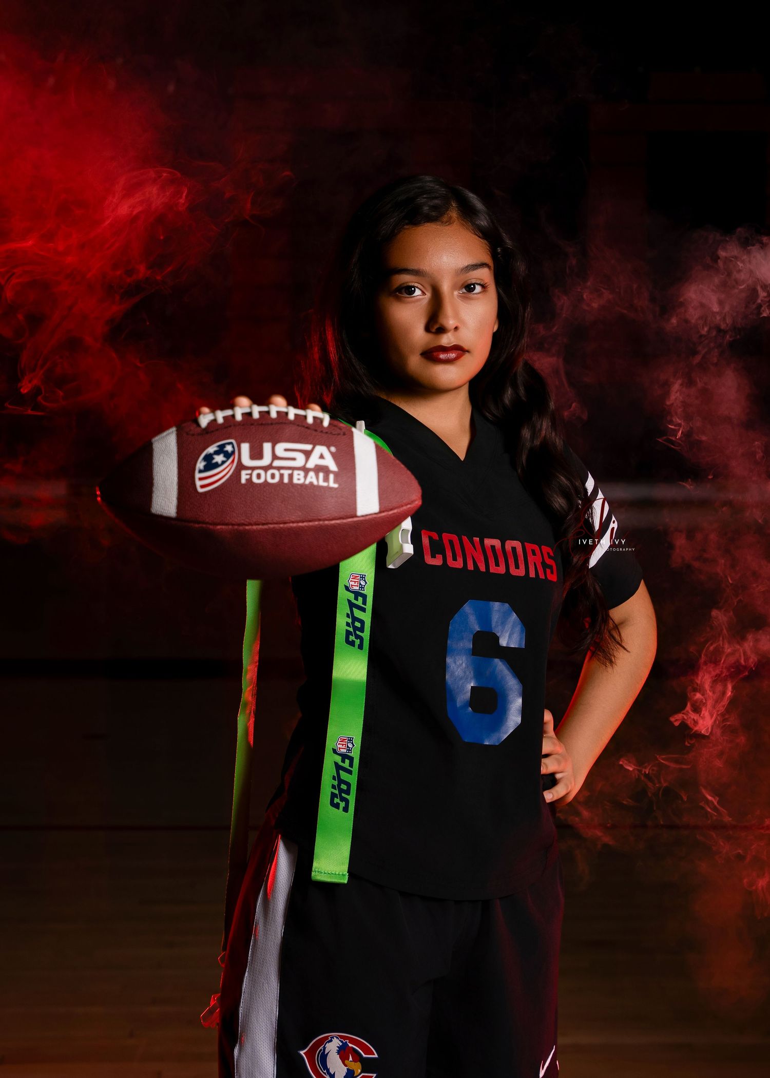 Football player in black uniform with green ribbons and USA Football logo against dark red smoky background.
