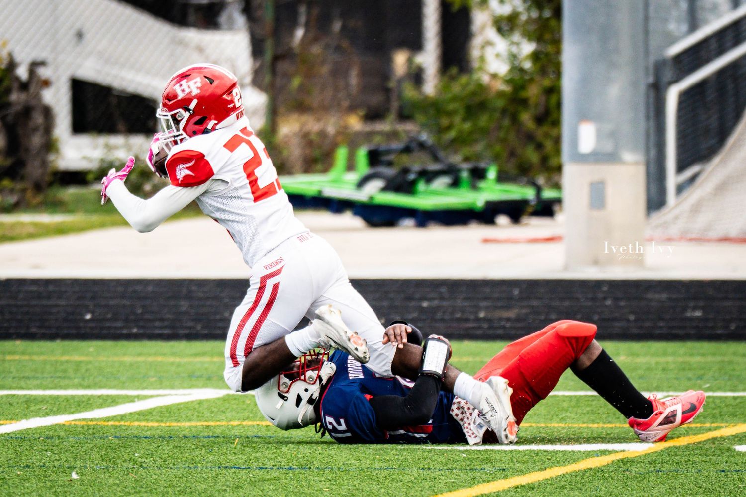 Multiple football players in red and blue uniforms spread across a green turf field during a game.