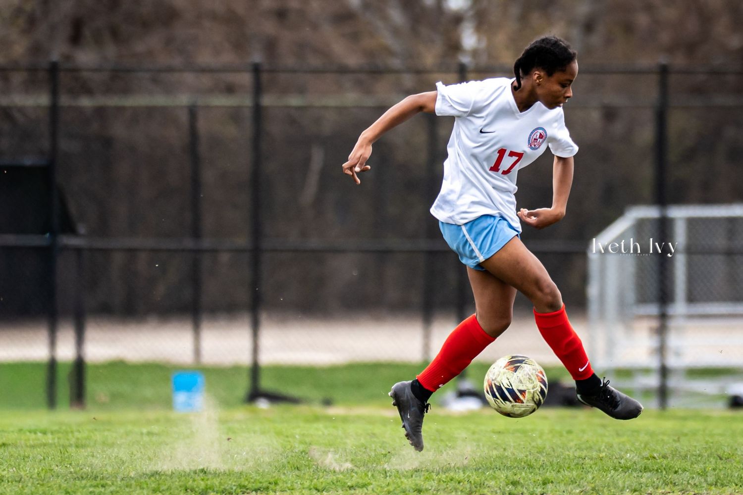 Soccer player #17 in white and red uniform dribbles ball on green field during outdoor match.