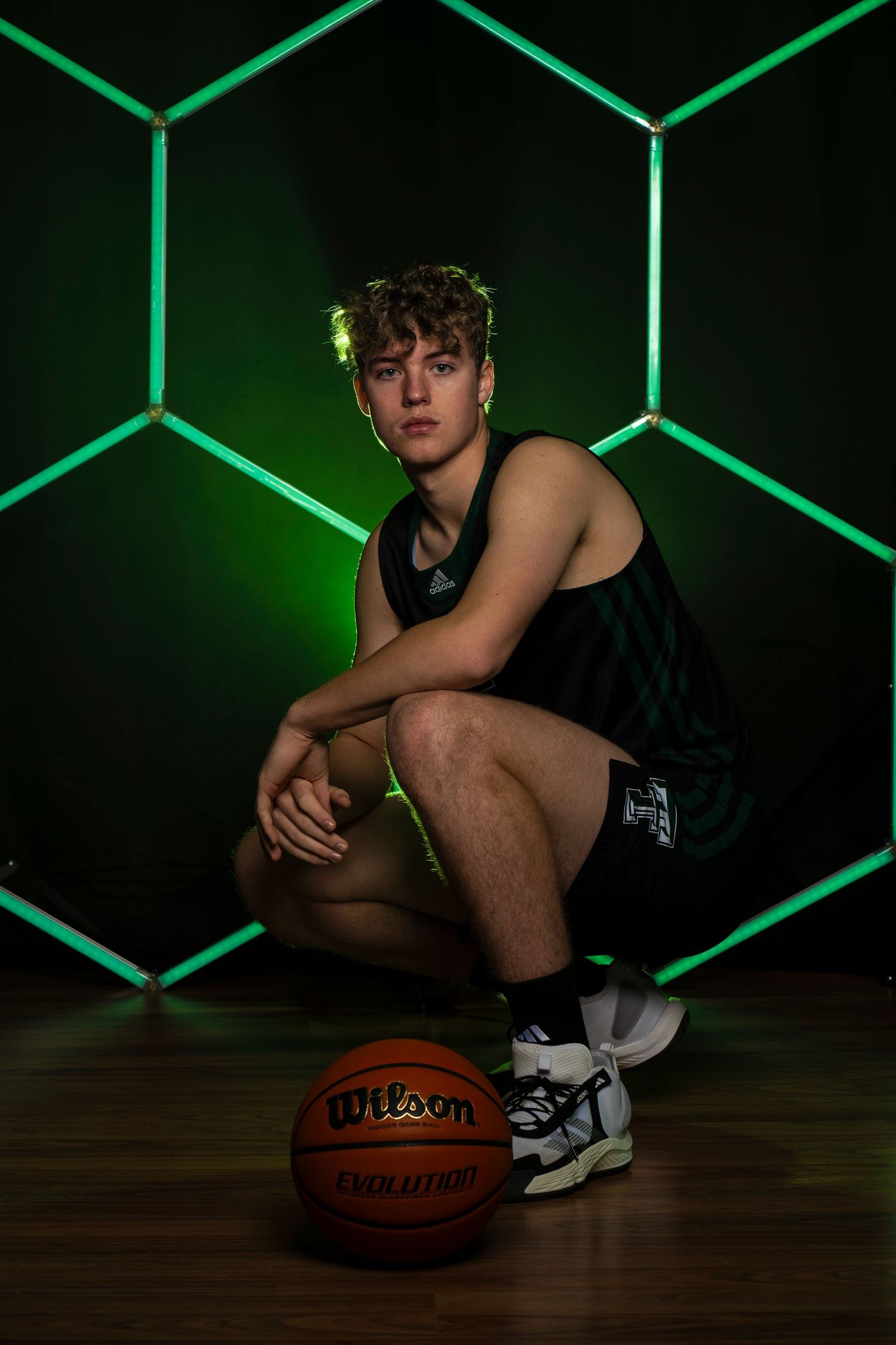 Low angle shot of athlete seated with basketball on floor with green geometric lighting.