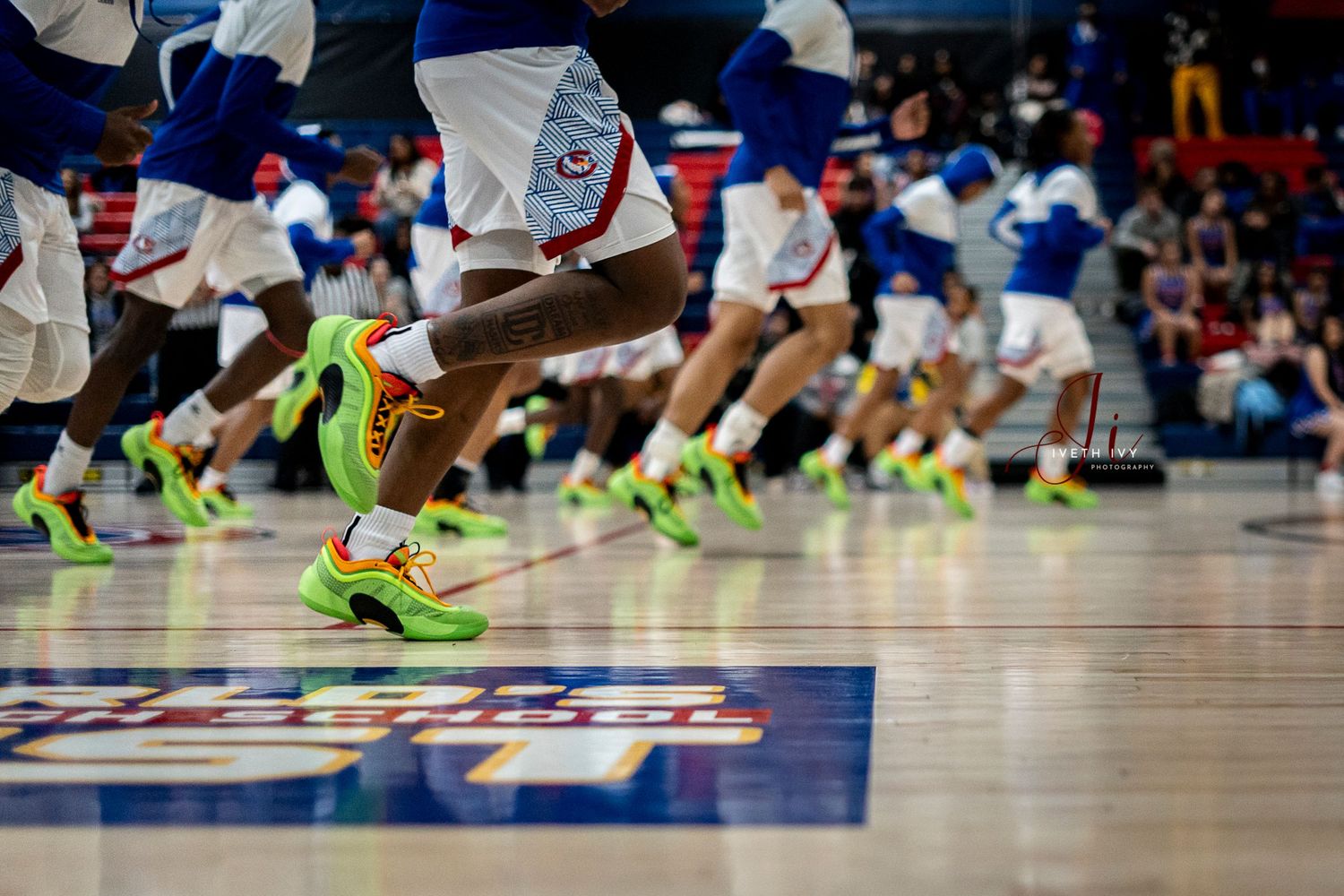 Basketball players in bright yellow sneakers jump in synchronized motion on a blue court during an indoor game.