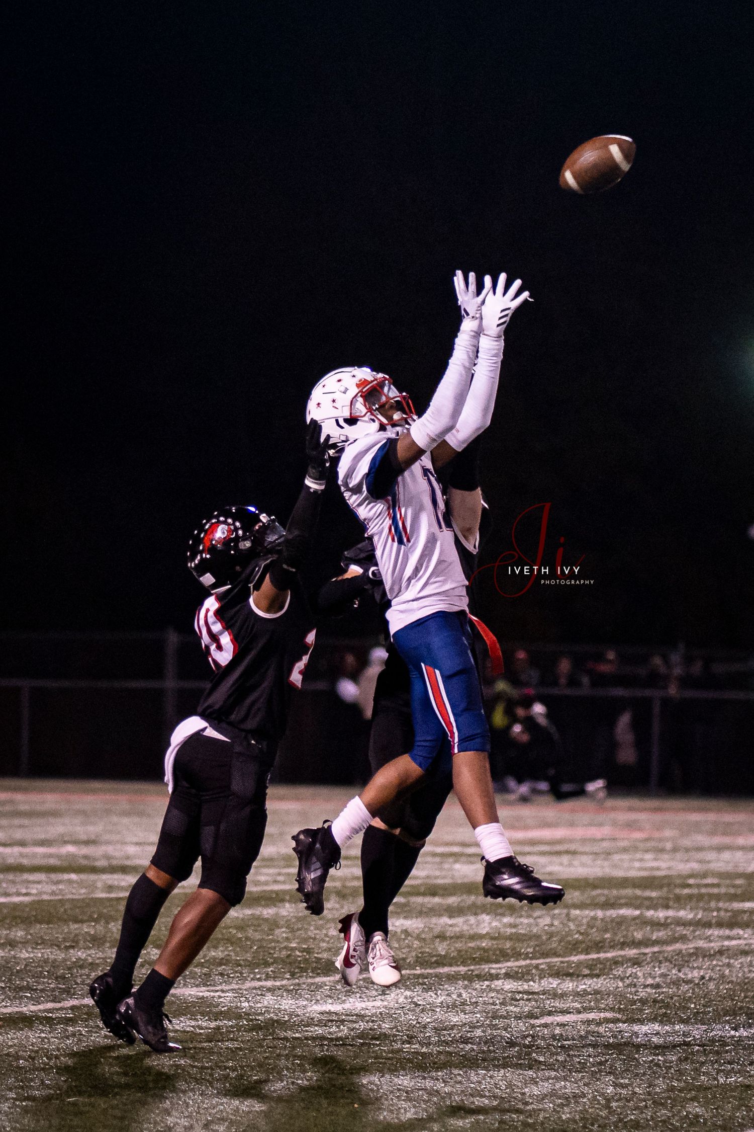 Athletes playing football in a nighttime game dive for a loose ball on a snowy field under stadium lights.