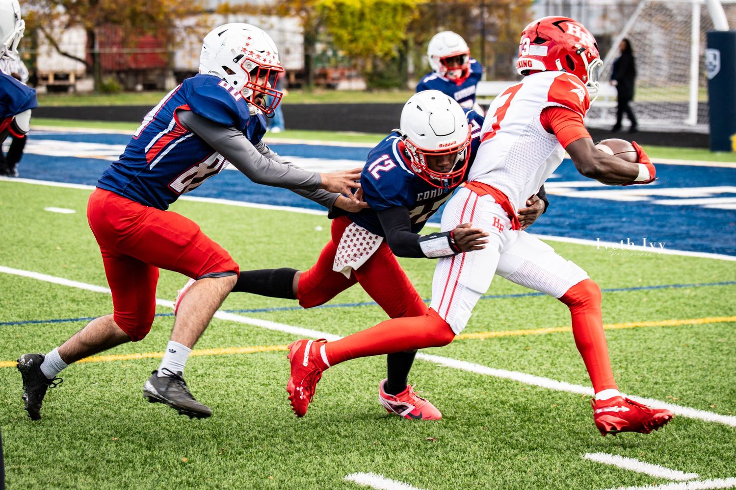 Football players dive and stretch during an intense play on the field in red and blue uniforms.
