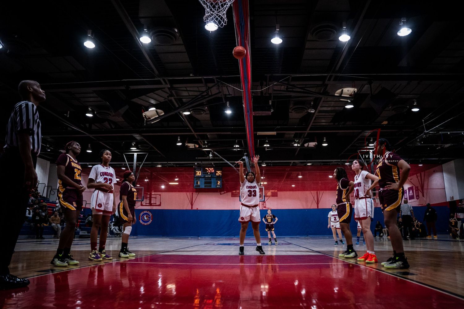 Basketball players compete on an indoor court during gameplay with spectators watching from the sidelines.