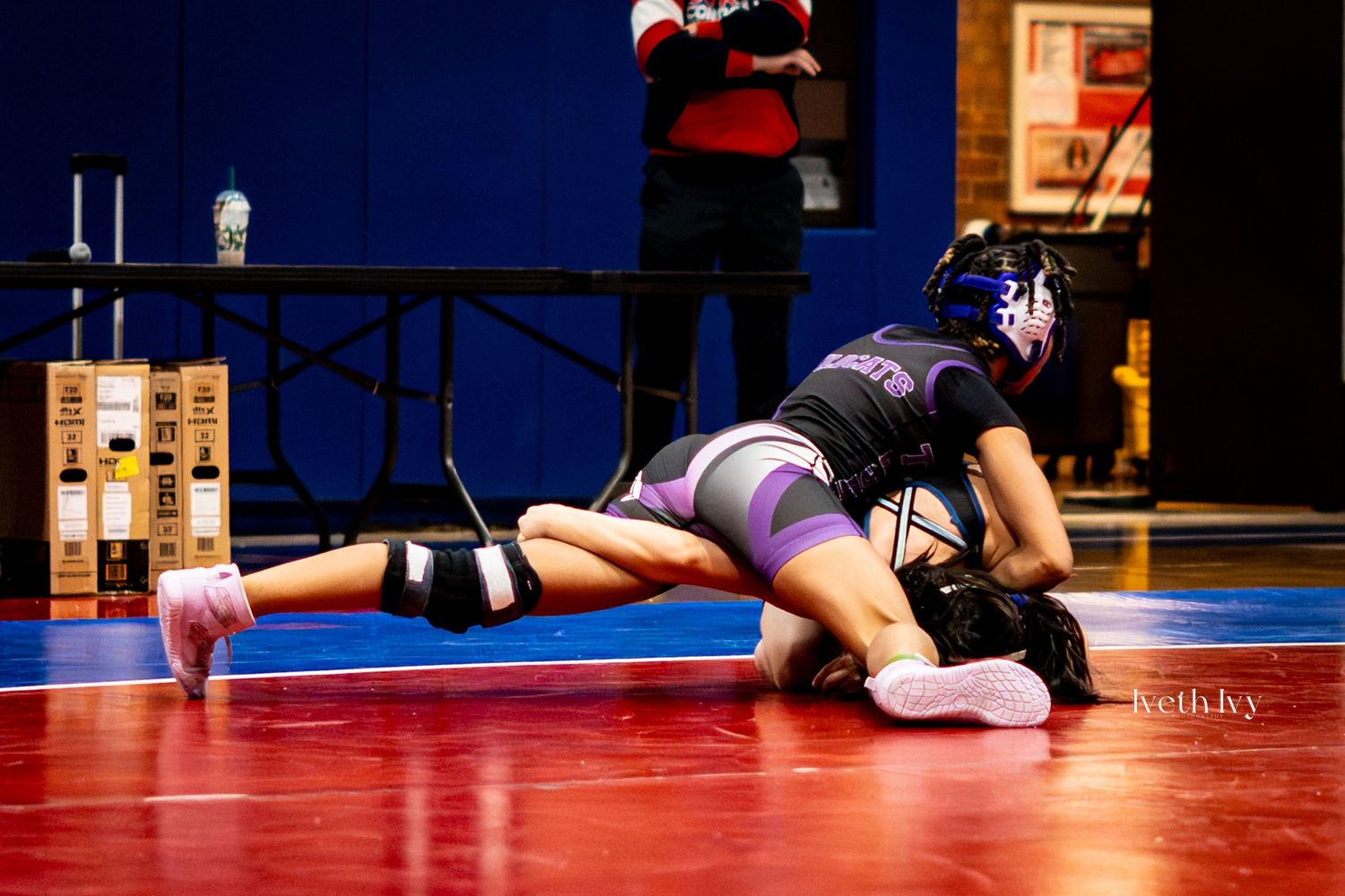 Multiple wrestlers lie on red and blue mats during a wrestling tournament.
