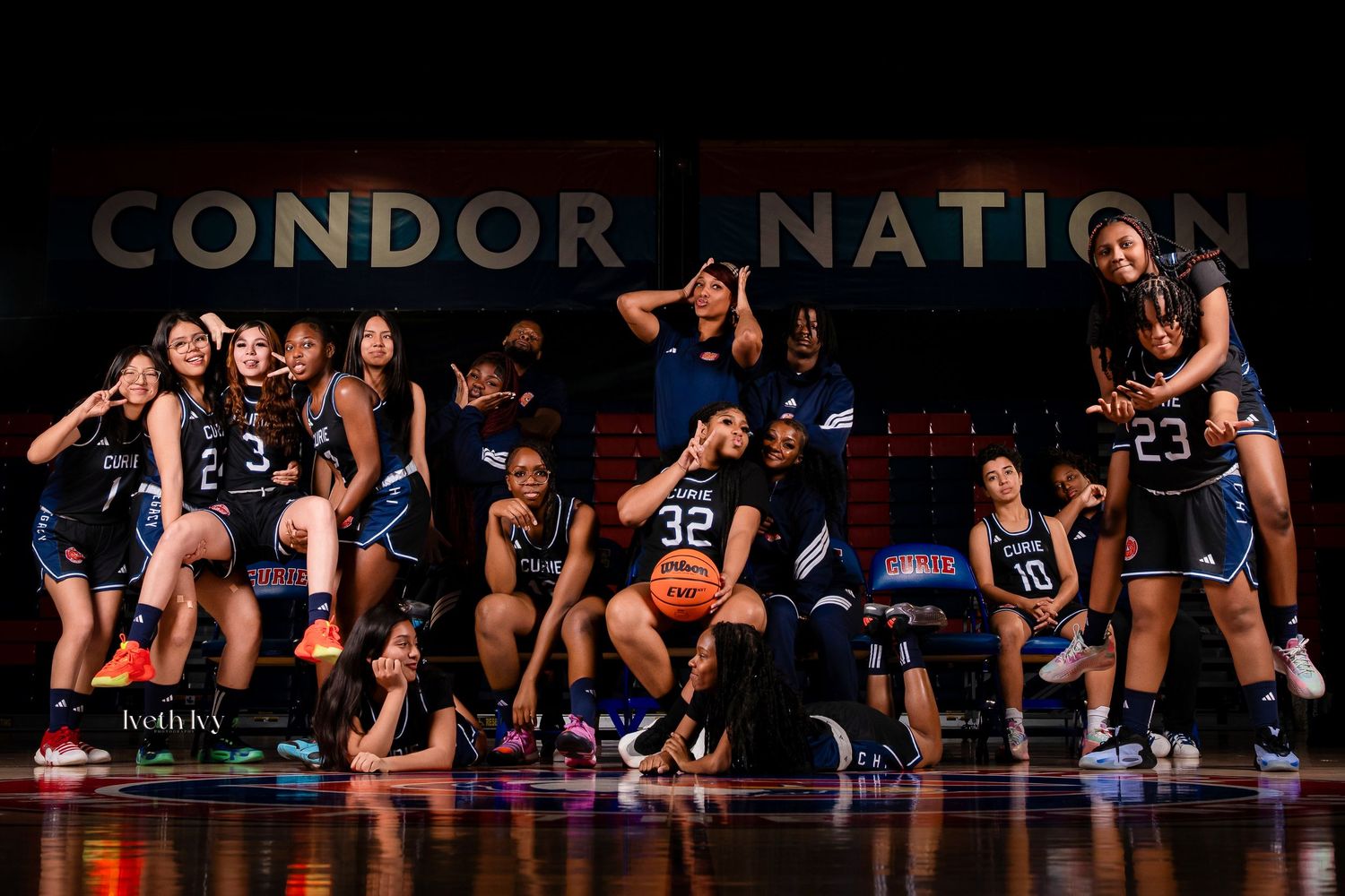 Basketball players in dark uniforms lie on the court floor in a synchronized formation during a performance.