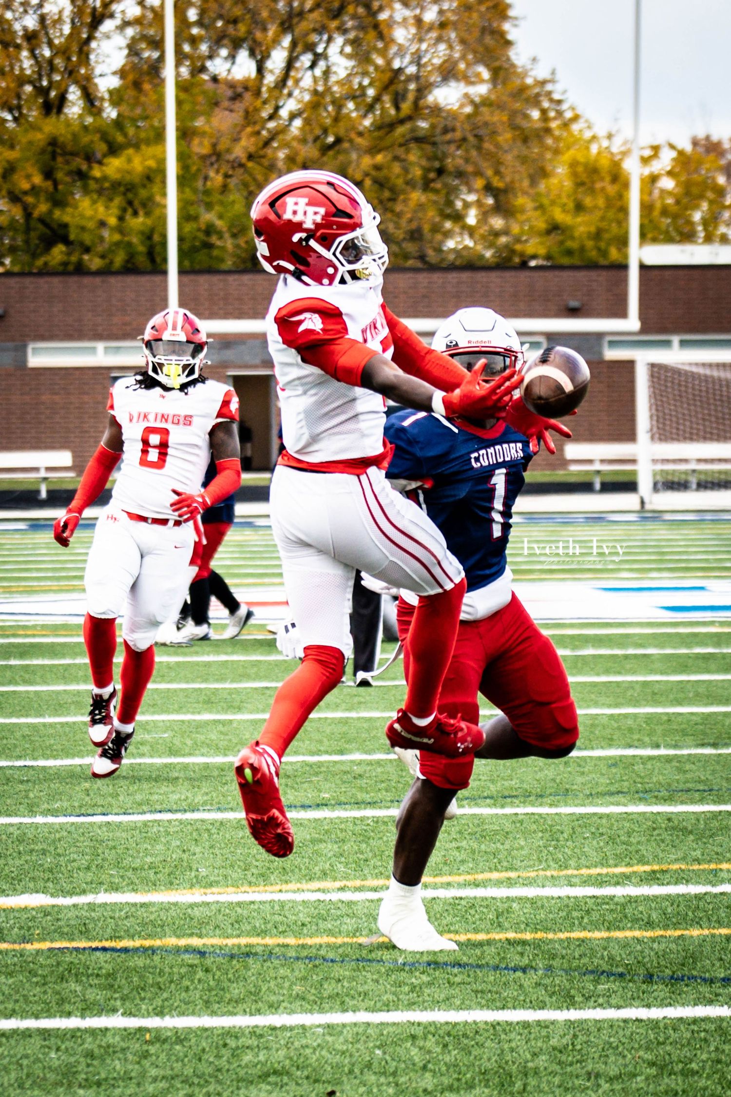 Football player in red uniform makes an acrobatic diving catch attempt on the field during a game.
