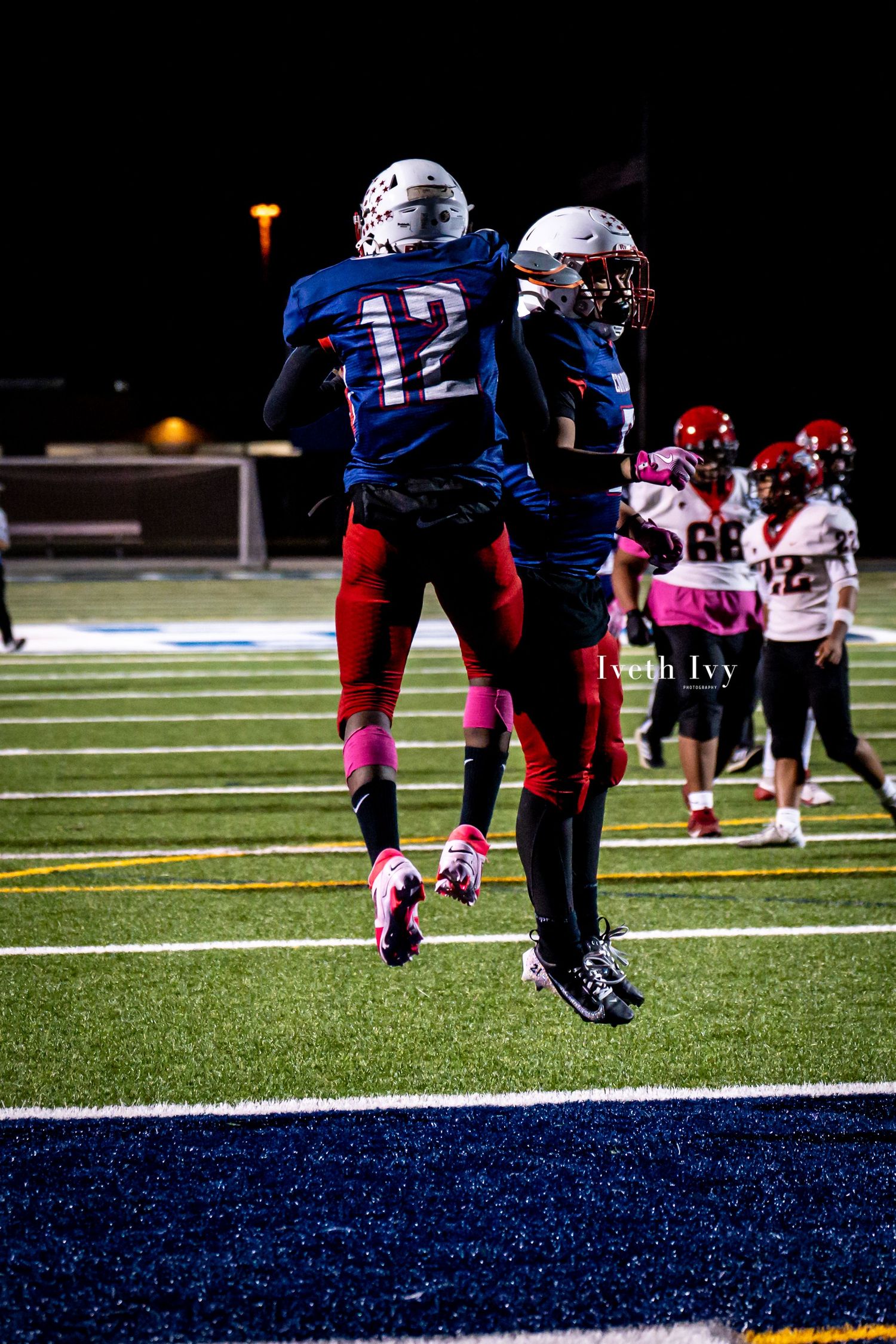Football players celebrate with a jump celebration in the end zone during a nighttime game.