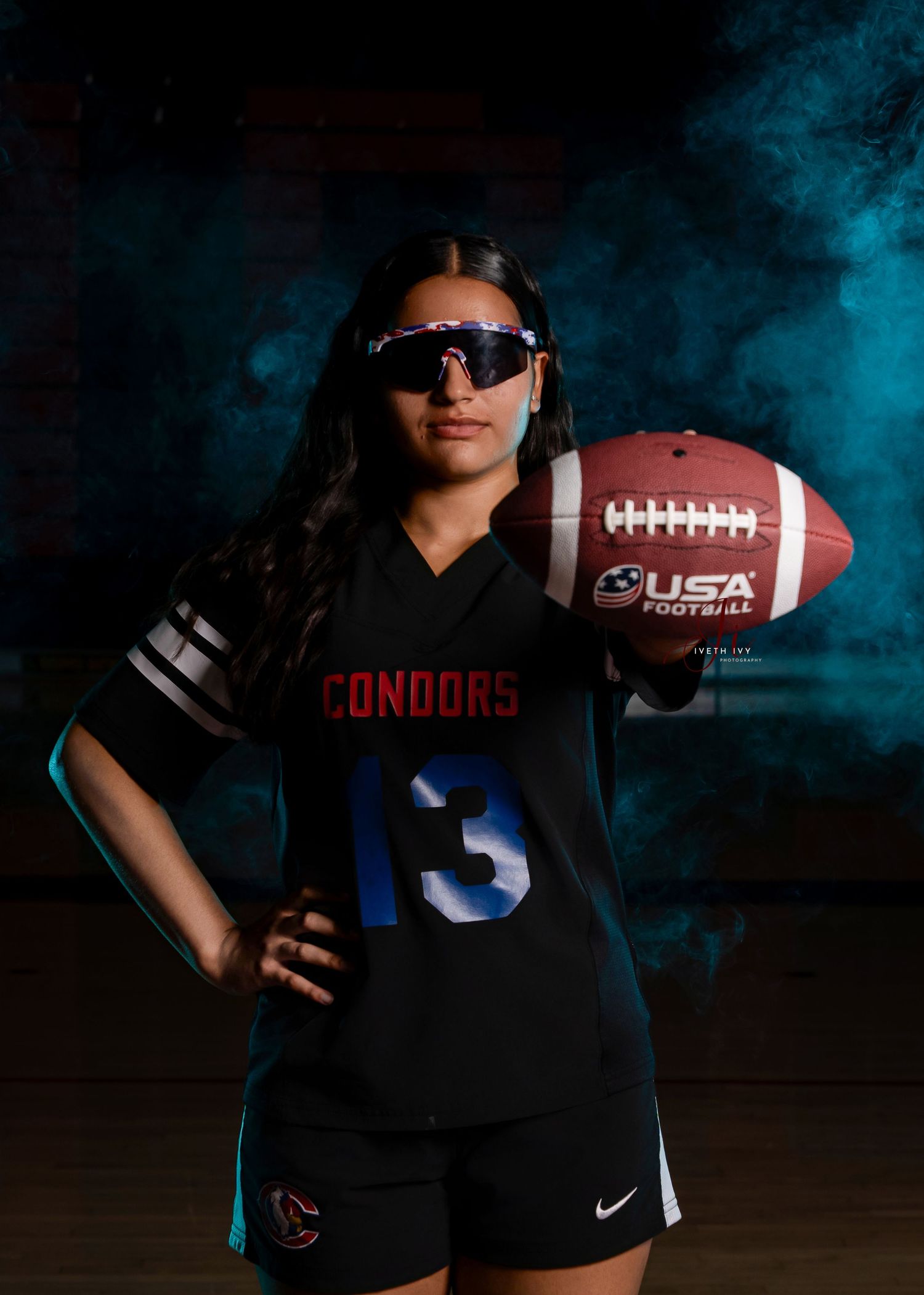 Athlete in black jersey with number 13 poses with football in moody blue lighting for sports portrait.