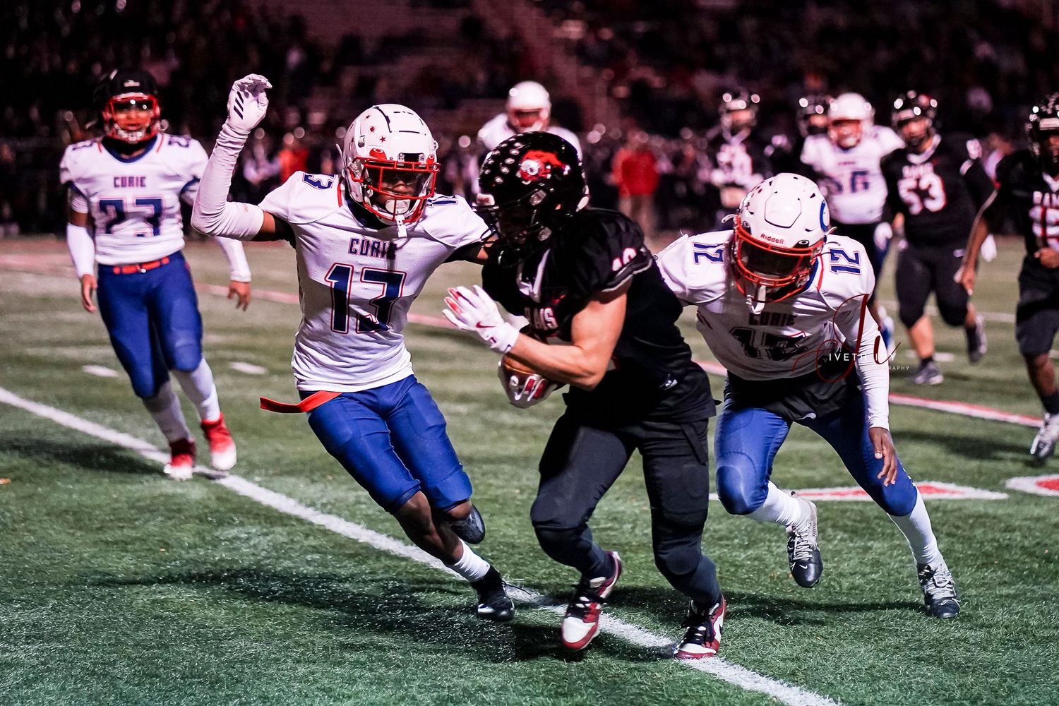 High school football players compete for the ball during an intense nighttime game on a turf field.