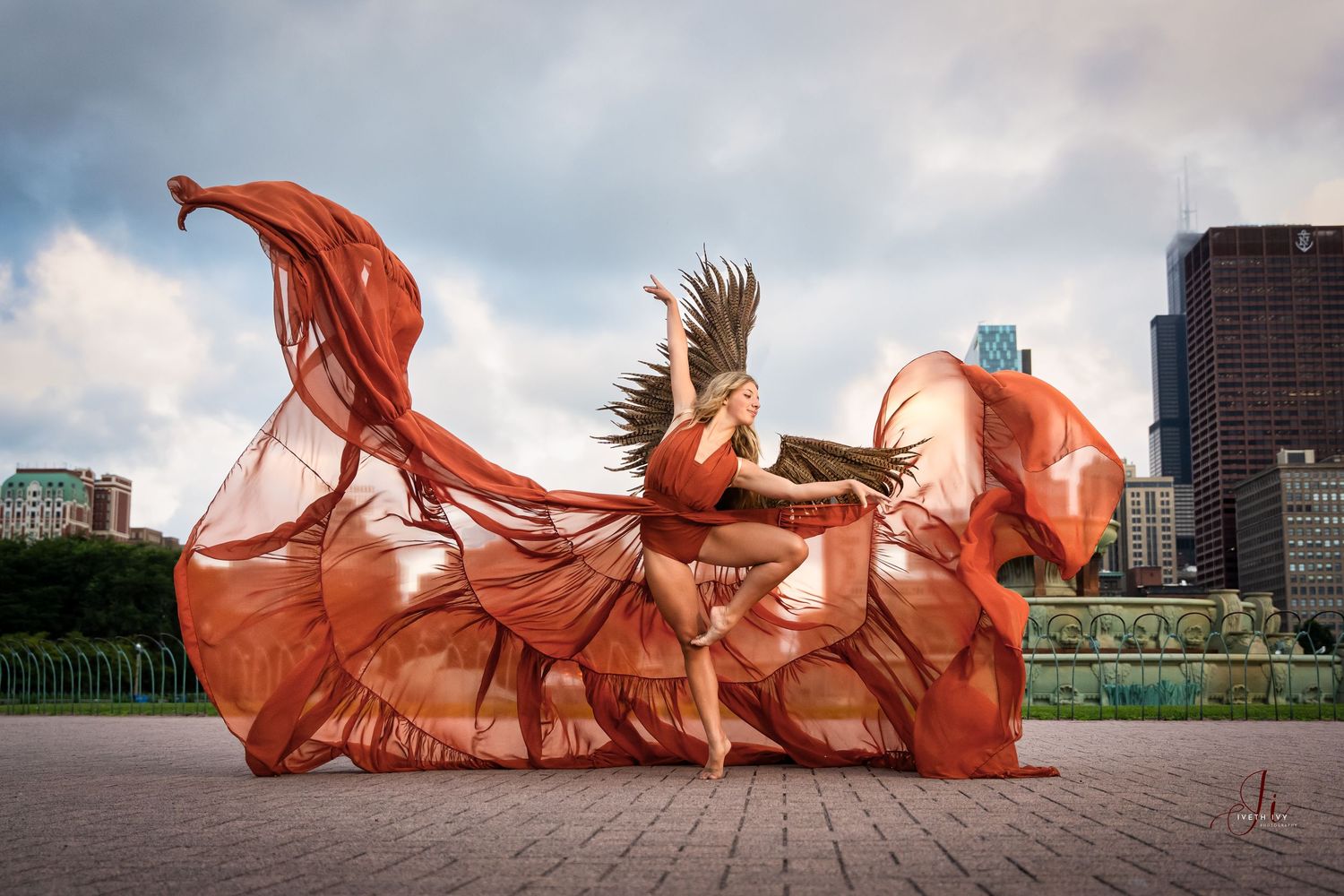 A flowing terracotta-colored fabric billows and dances dramatically against an urban skyline background.