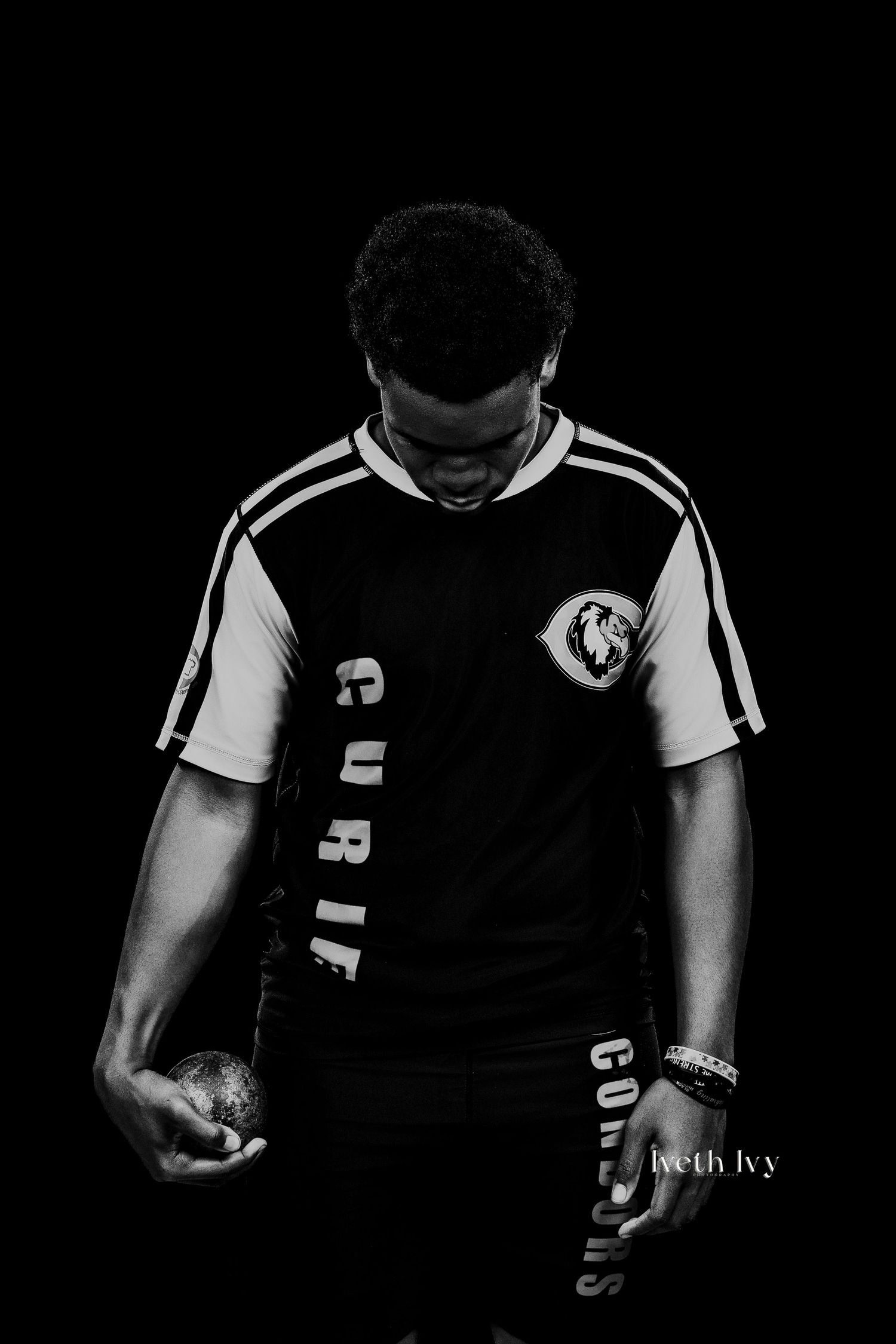 Black and white portrait of a young man in a sports jersey holding a ball, dramatic studio lighting.