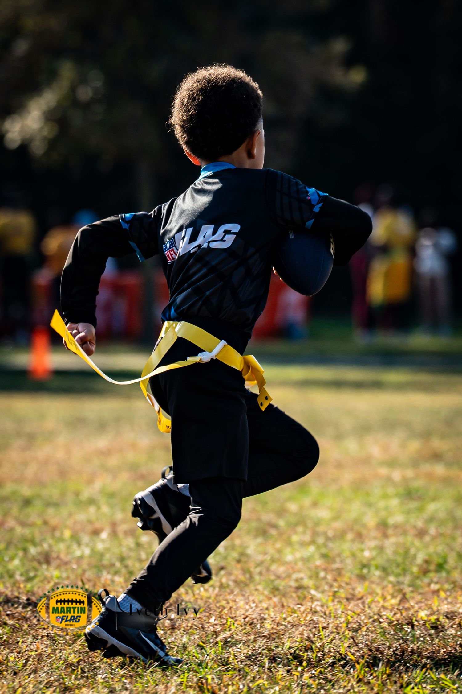 A person in black athletic wear plays flag football, reaching for yellow flags on a sunny autumn field.