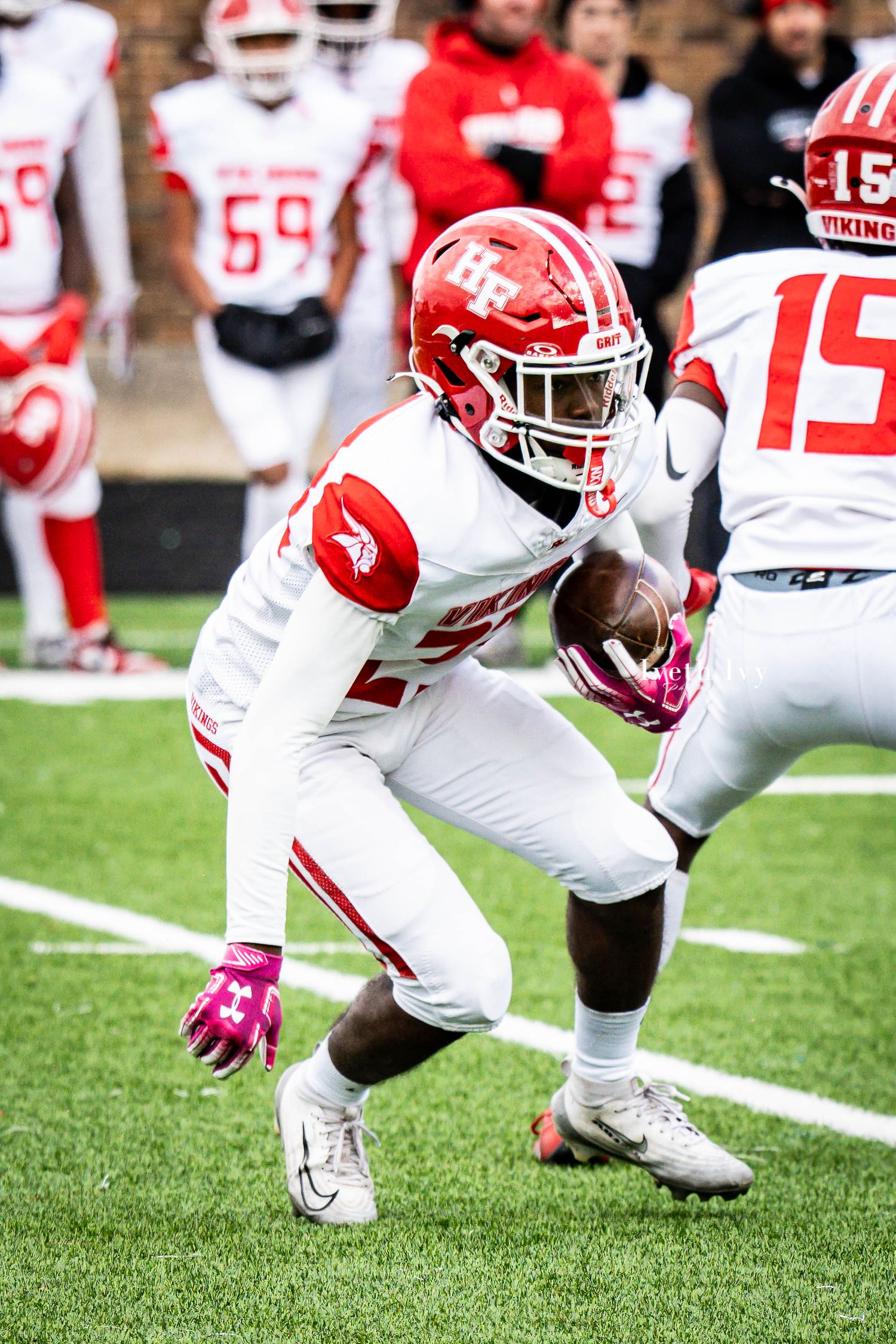 Football players in red and white uniforms crouch in defensive positions on a green turf field during a game.