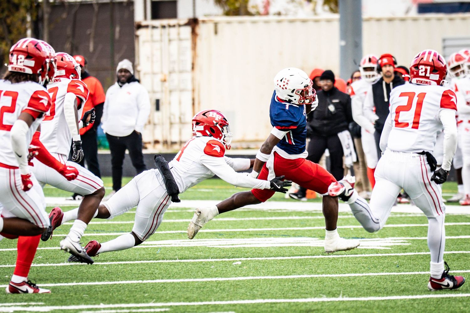 Football players from opposing teams in red and blue uniforms line up for a play on the field.
