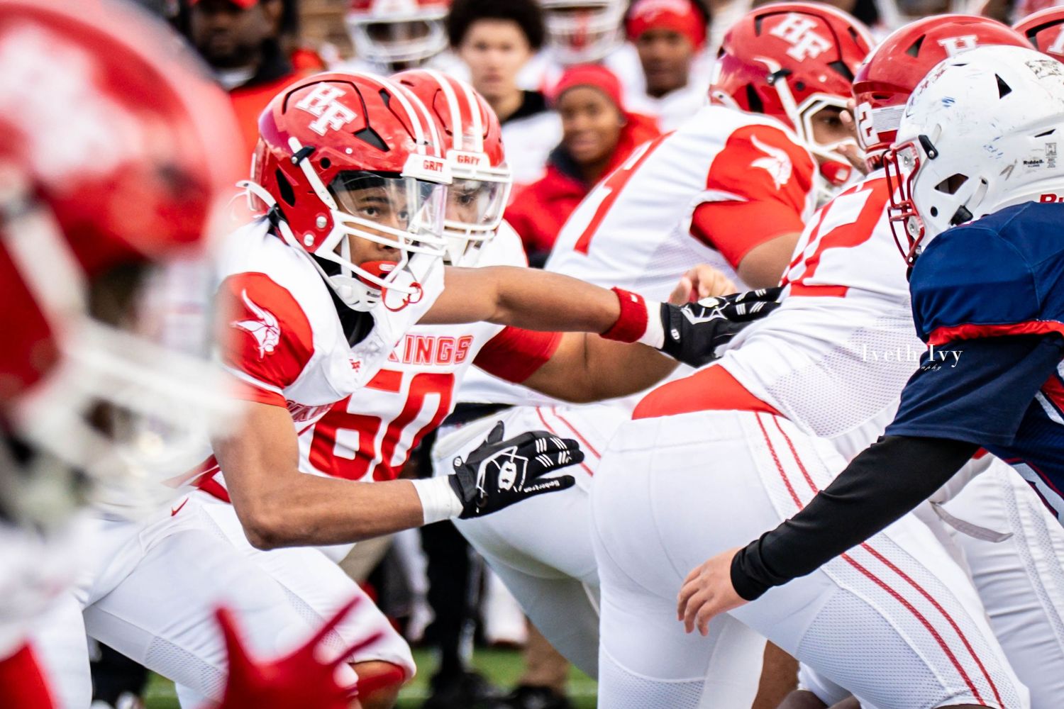 College football players in red and white uniforms battle at the line of scrimmage during an intense game.