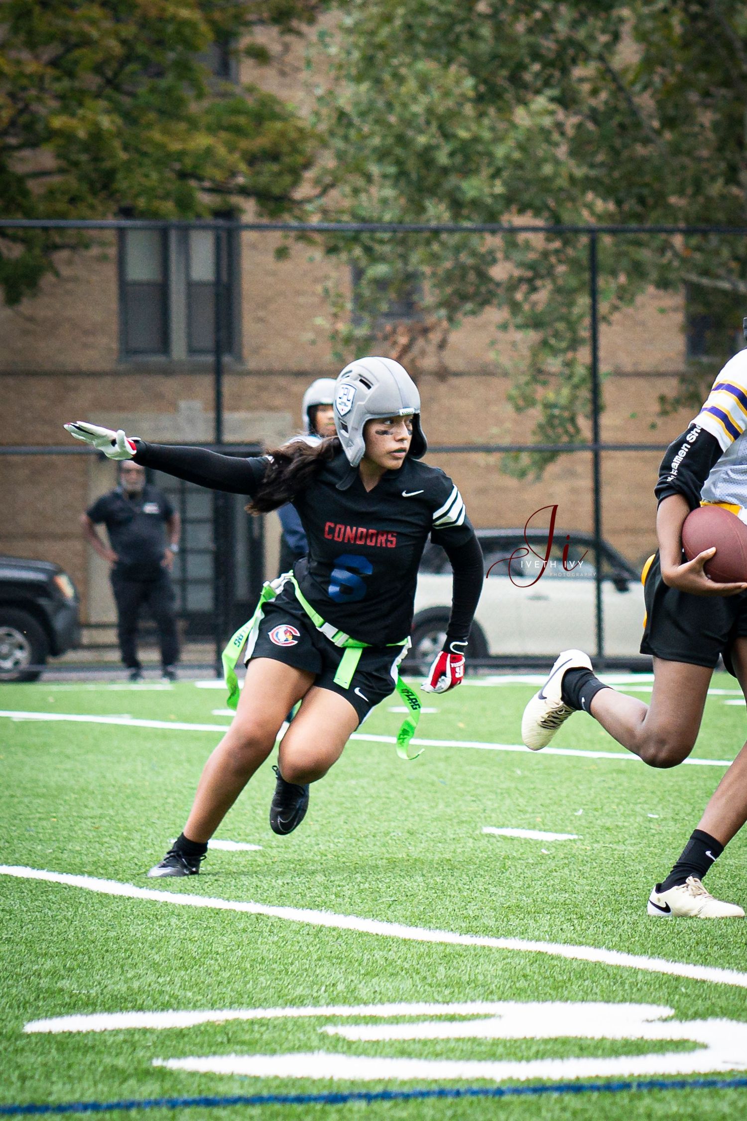 Flag football player in white helmet and black uniform runs with arm outstretched on turf field during game action.