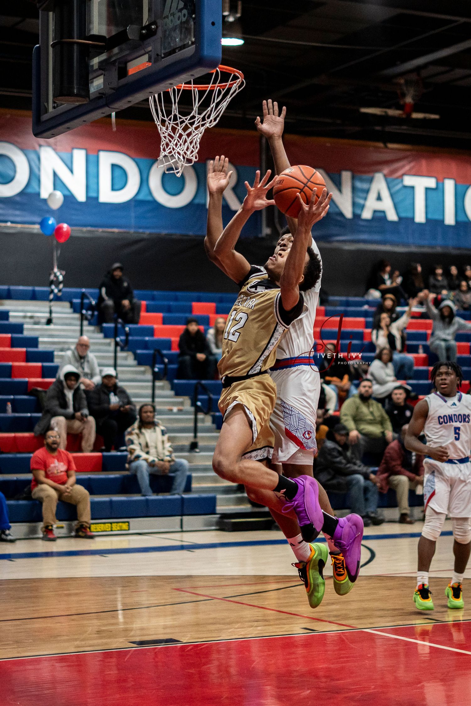 Basketball players leap high during an intense game on the court with red and blue stadium colors in the background.