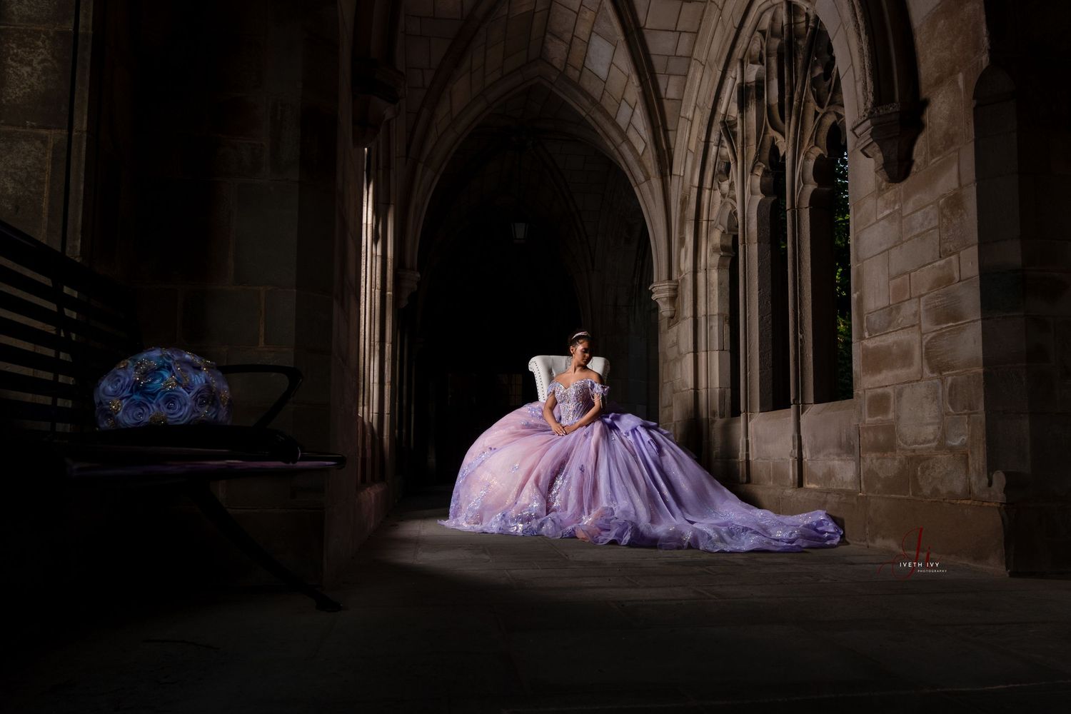 A figure in a lavender ball gown sits gracefully in a gothic cathedral corridor with dramatic lighting and arched architecture.