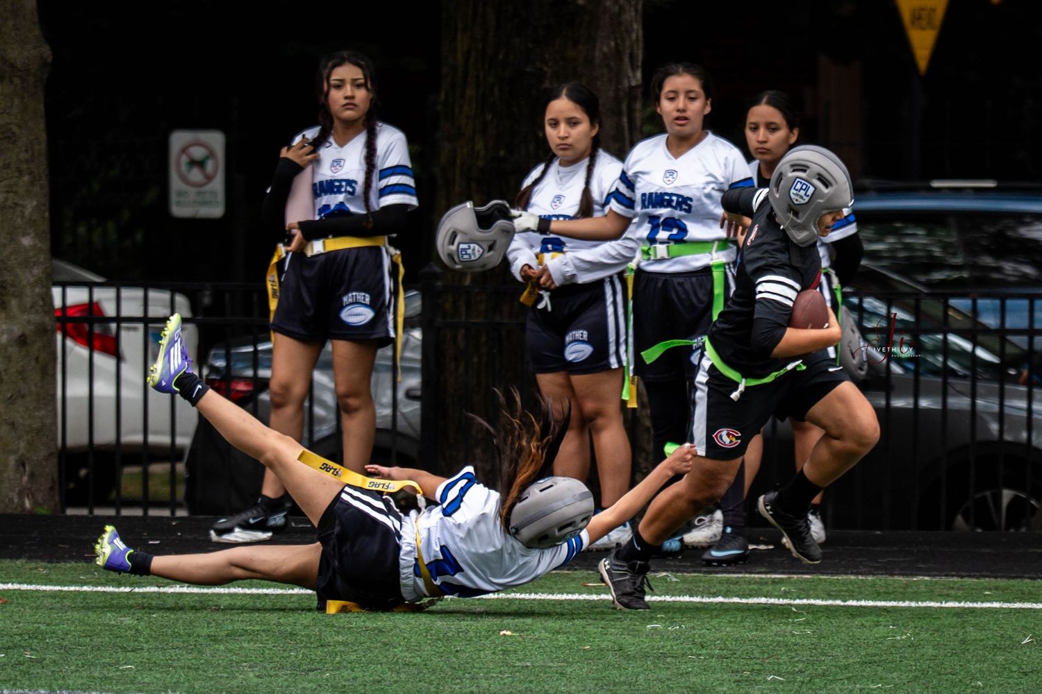 Soccer players rest and stretch on the sidelines of a turf field during a break in the game.