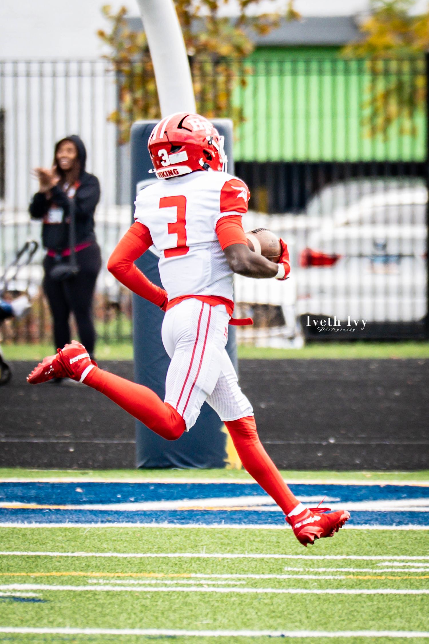 Football player in red and white uniform runs with the ball across a blue turf field during a game.