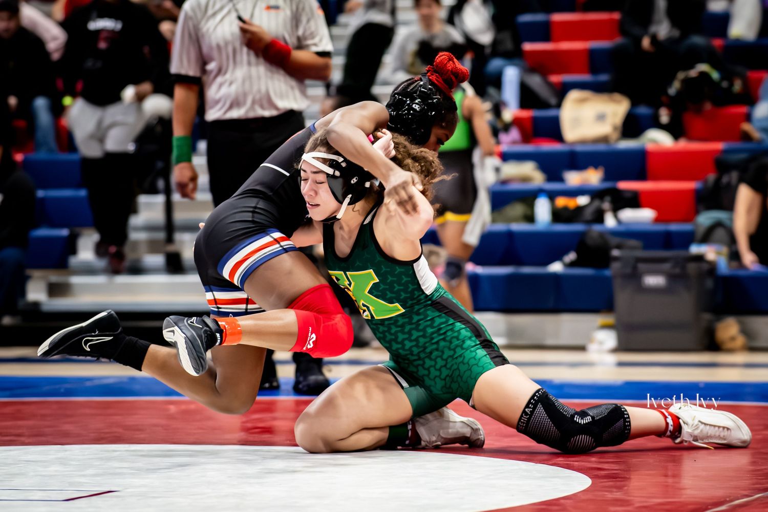 Two wrestlers compete in an intense match on a red and blue mat during a high school wrestling competition.