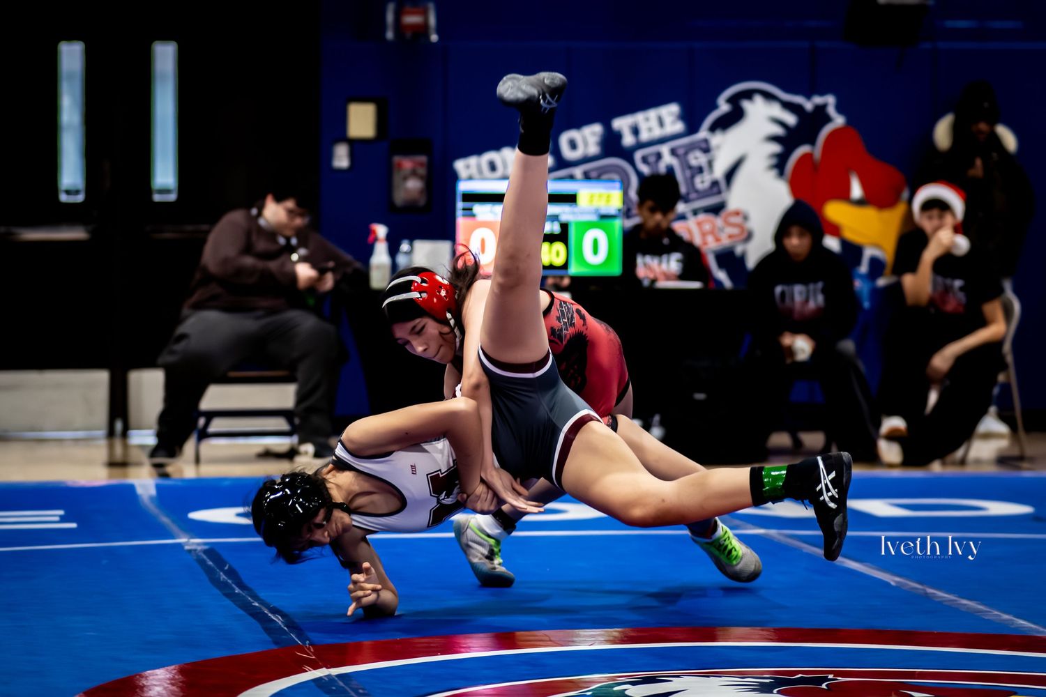 Wrestling competitors battle for position during an indoor tournament match on blue mats.