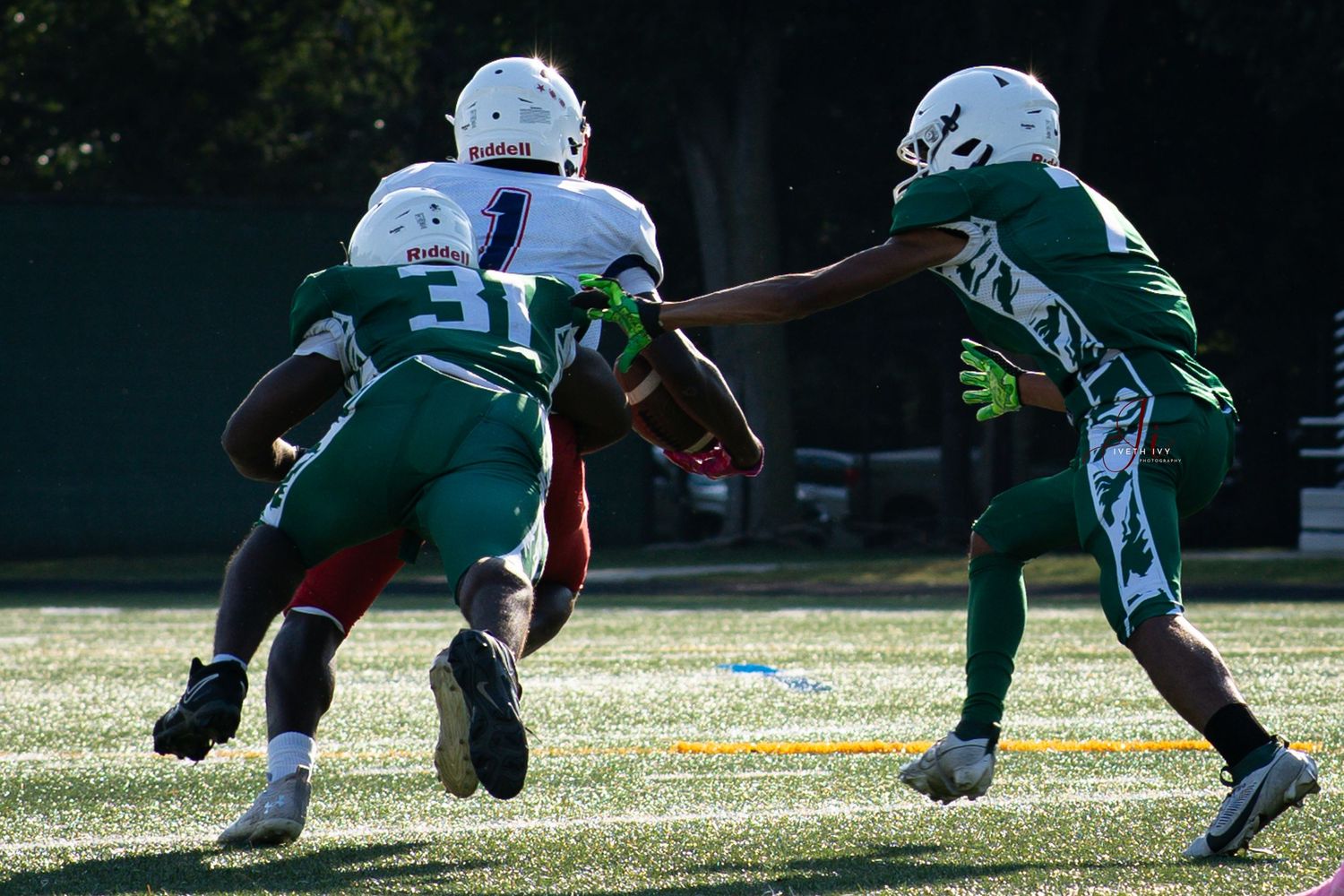 Football players in green and white uniforms compete during a game on a sunny field.