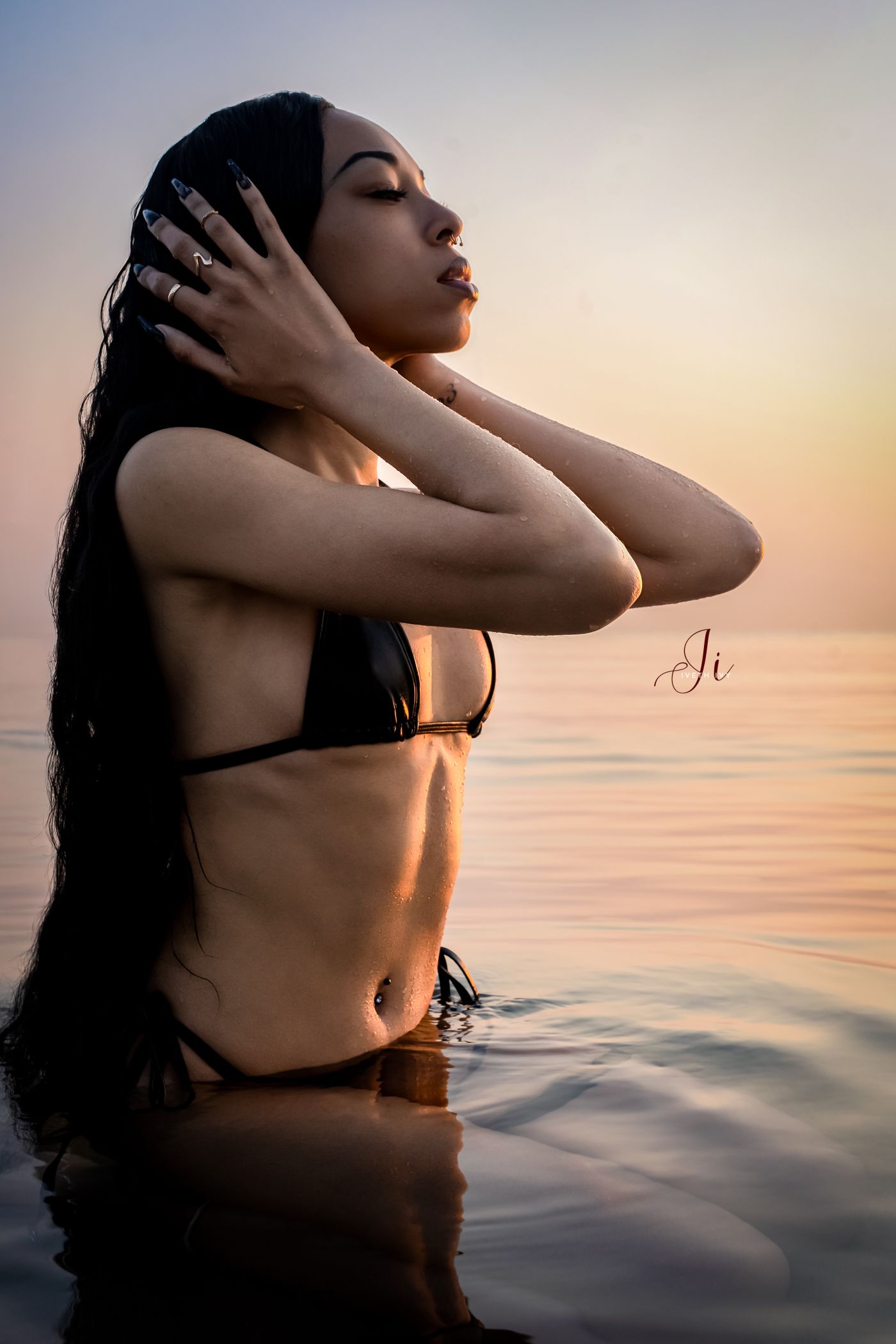 Silhouetted figure bathing in tranquil ocean waters during golden sunset with glowing sky reflections on calm surface.