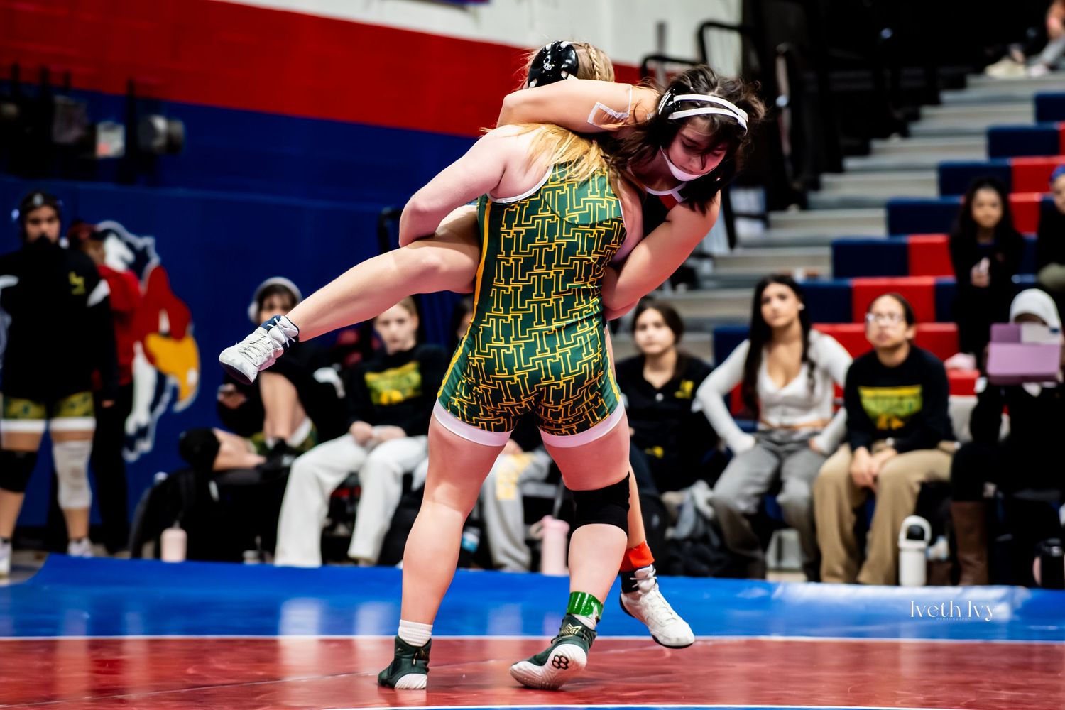 Two wrestlers compete in an intense match on a blue mat during a high school wrestling competition.