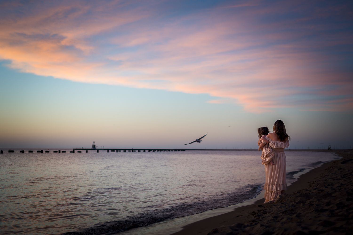 Beautiful coastal sunset over water with silhouettes gazing at the colorful pink and orange sky.