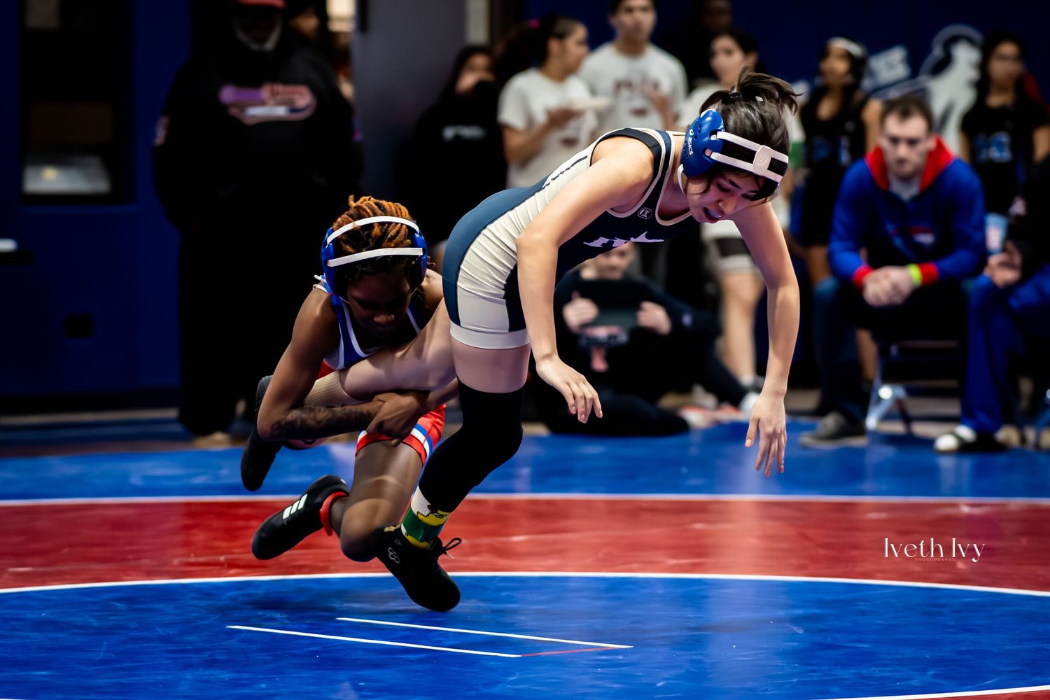 Wrestlers compete in a high school wrestling match on a blue mat during an intense grappling sequence.