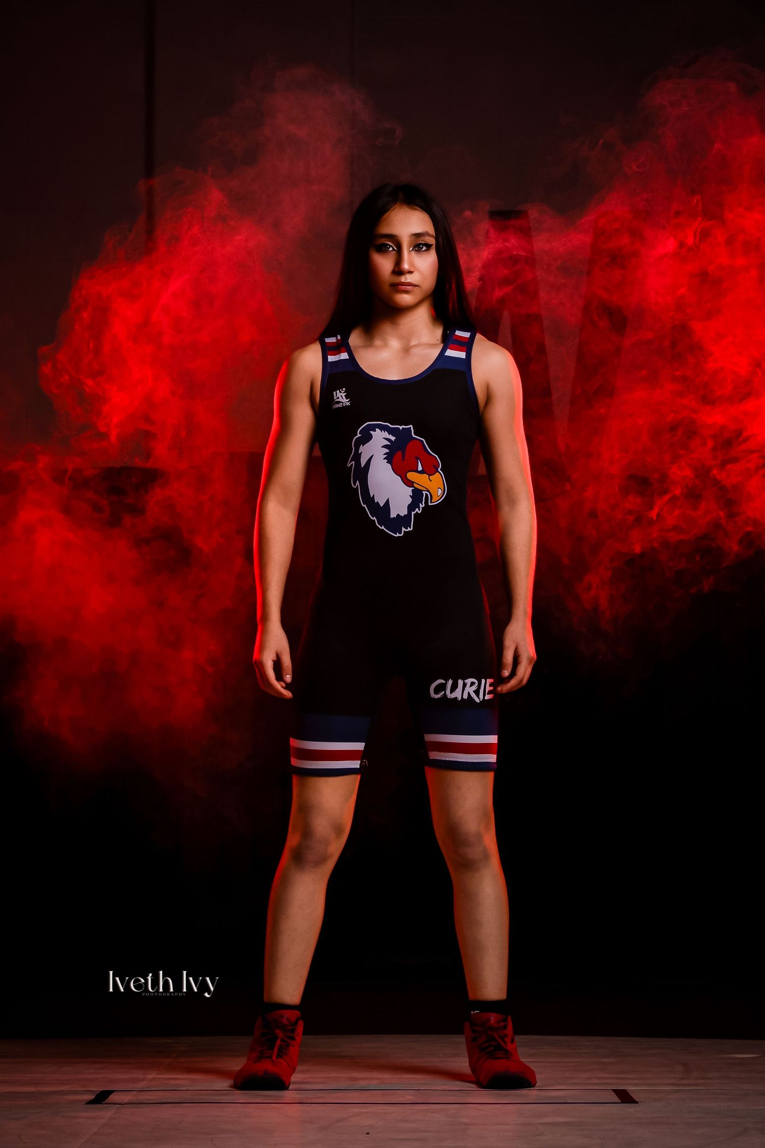 Athlete in black wrestling uniform stands confidently against dramatic red smoke background during sports photoshoot.