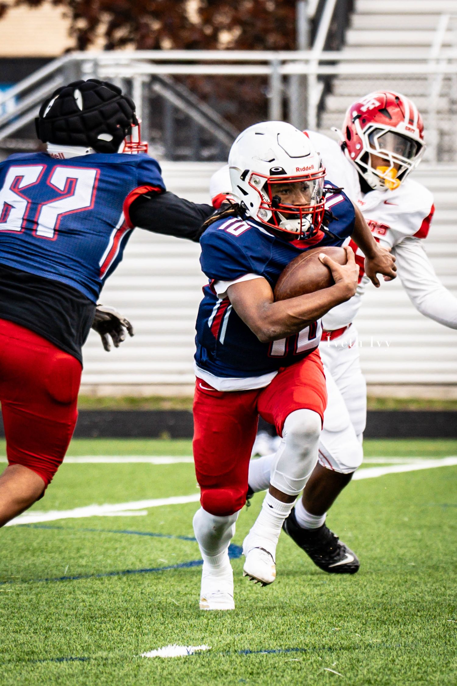 Football players in red and blue uniforms practice blocking drills on the field during training.